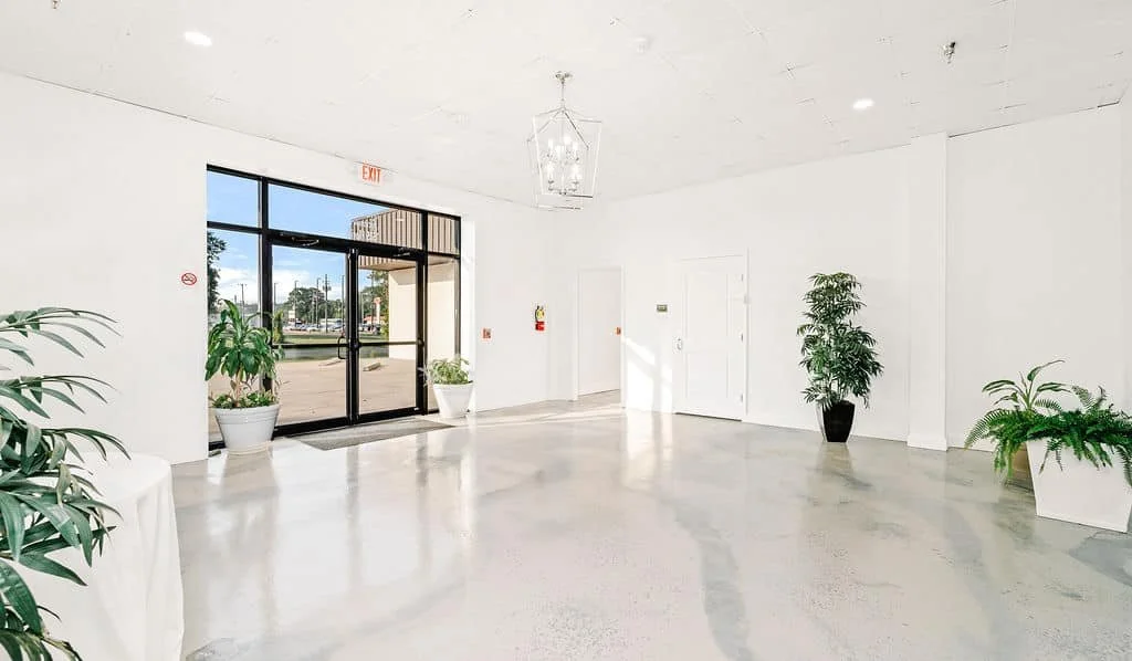 Empty white-walled lobby with potted plants, glass front door, and a chandelier.