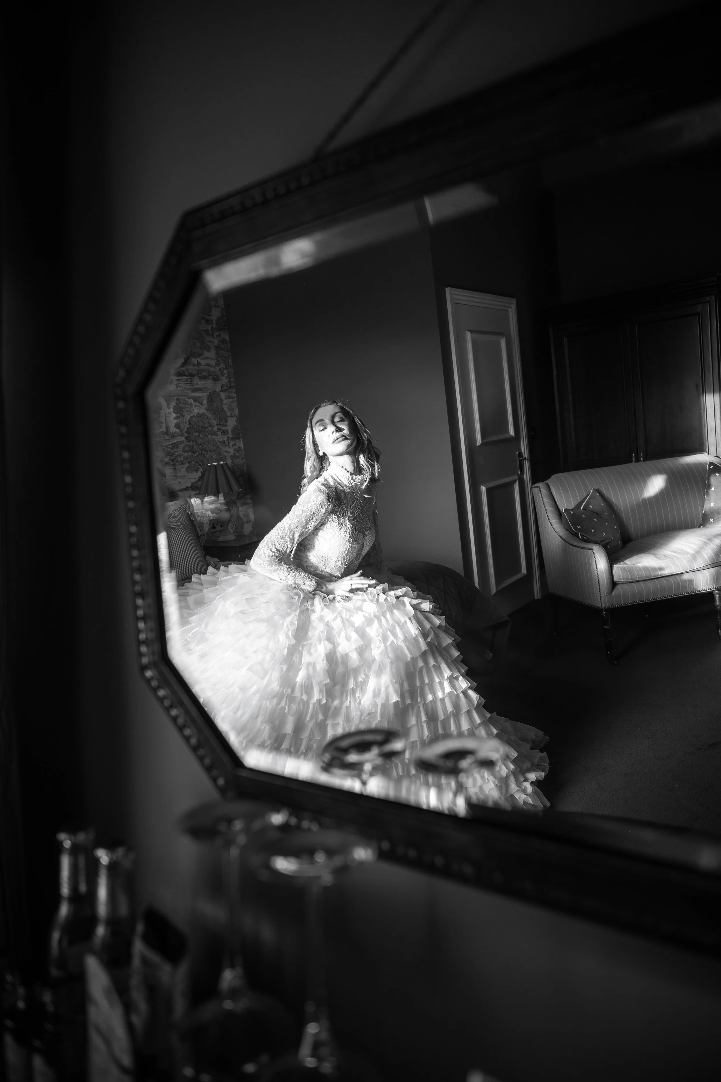 A bride captured through a mirror reflection as she adjusts her dress, surrounded by soft light and elegant vintage interiors at Cartmel Old Grammar House.