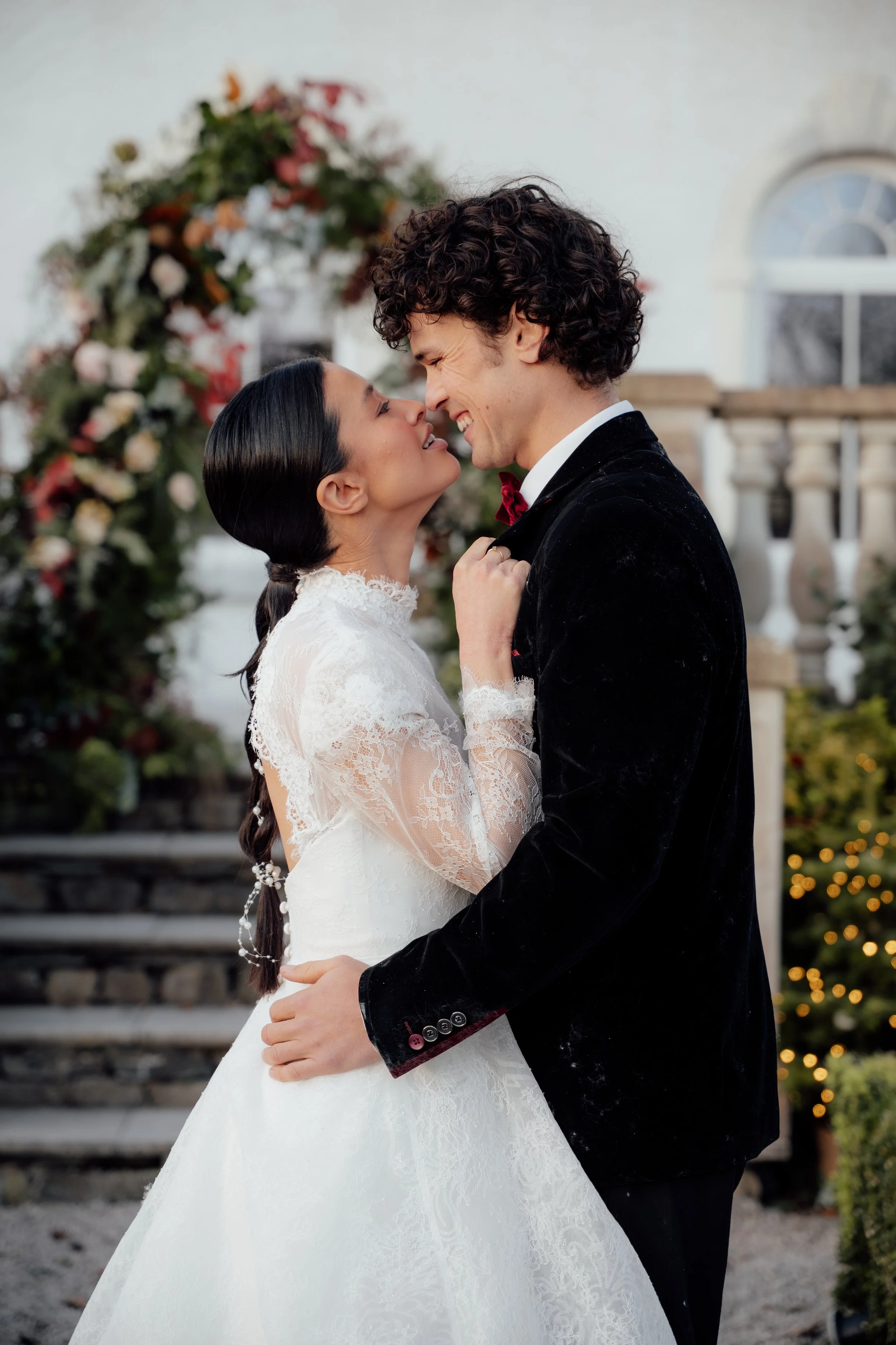 	
Bride and groom sharing a joyful, intimate moment at Cartmel Old Grammar House, standing beside a floral archway and stone steps.