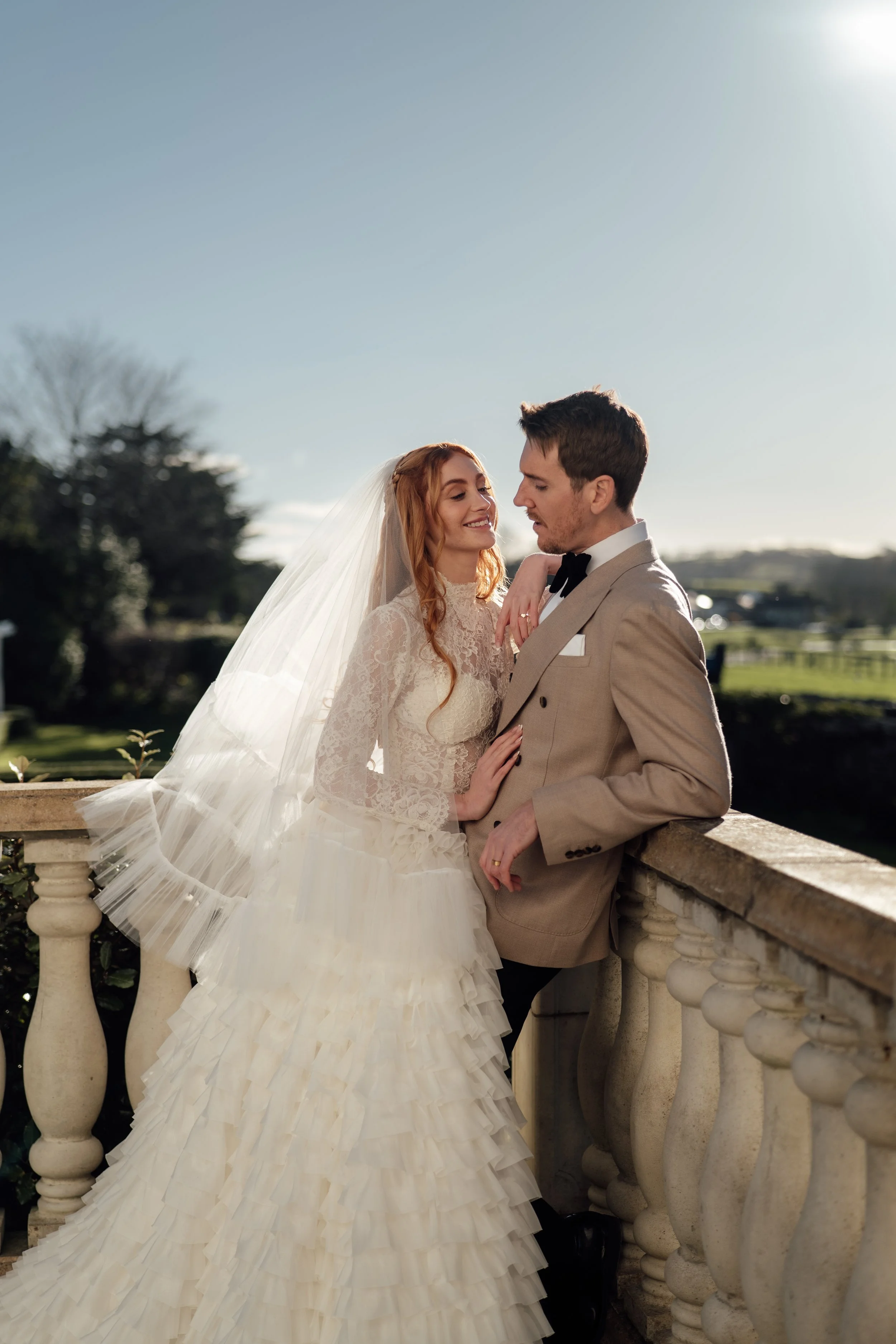 Bride and groom standing together on the terrace at Cartmel Old Grammar, captured in soft sunlight with elegant countryside views behind them.