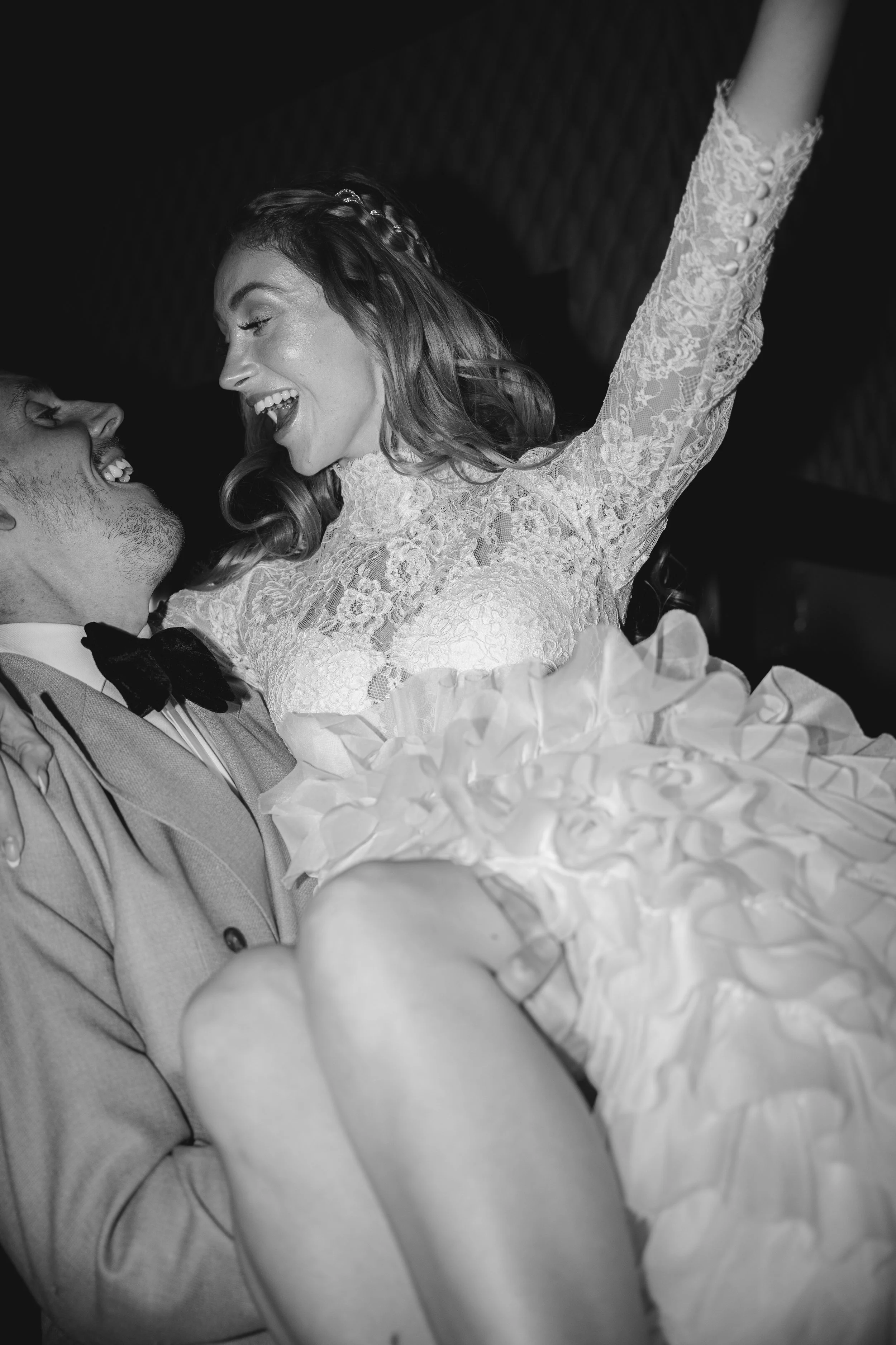 Black and white photo of a couple dancing closely, with the woman in a lace dress and the man in a suit, smiling and looking at each other.