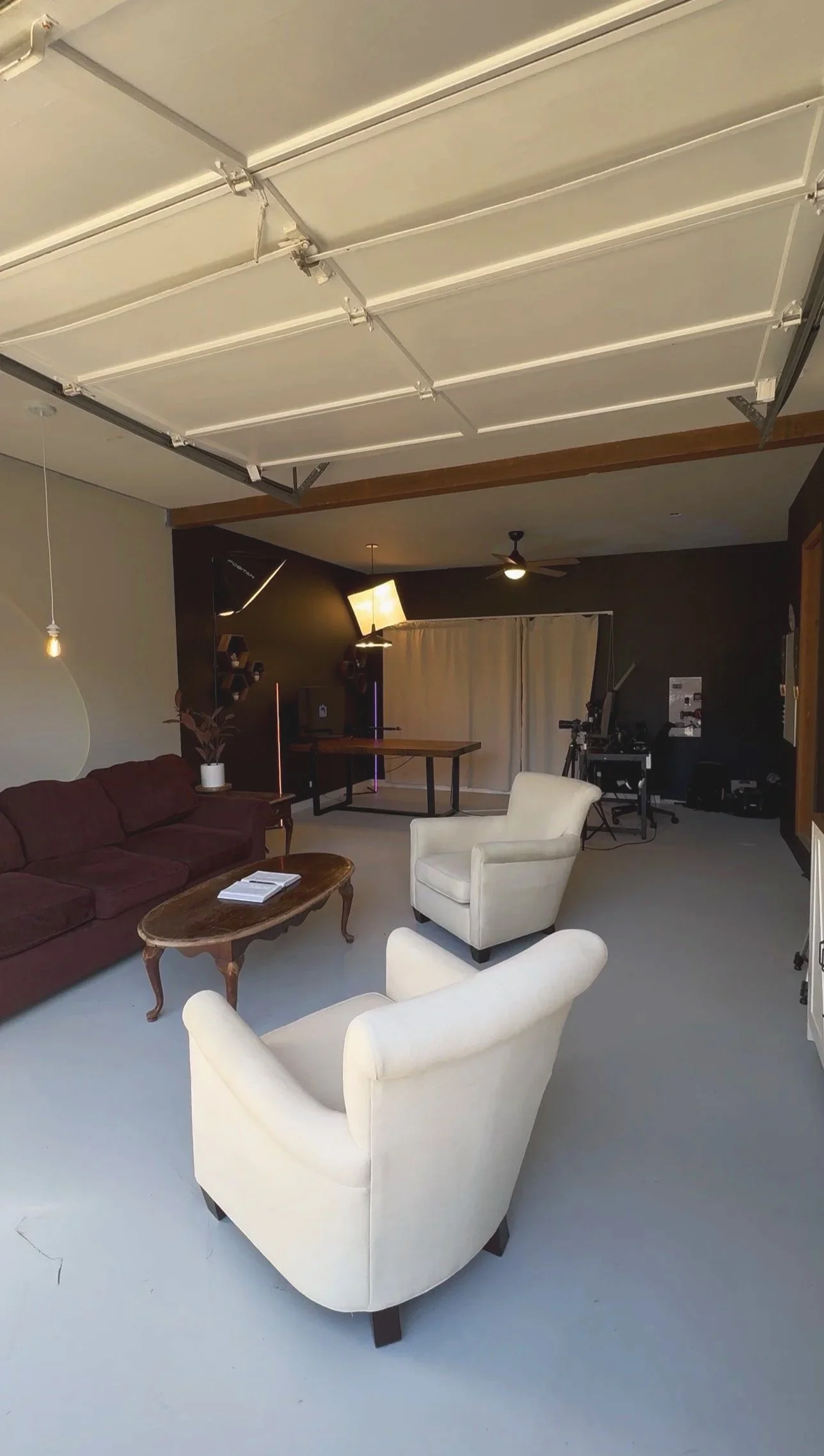 Podcast studio seating with a white armchair, burgundy sofa, and wooden coffee table.