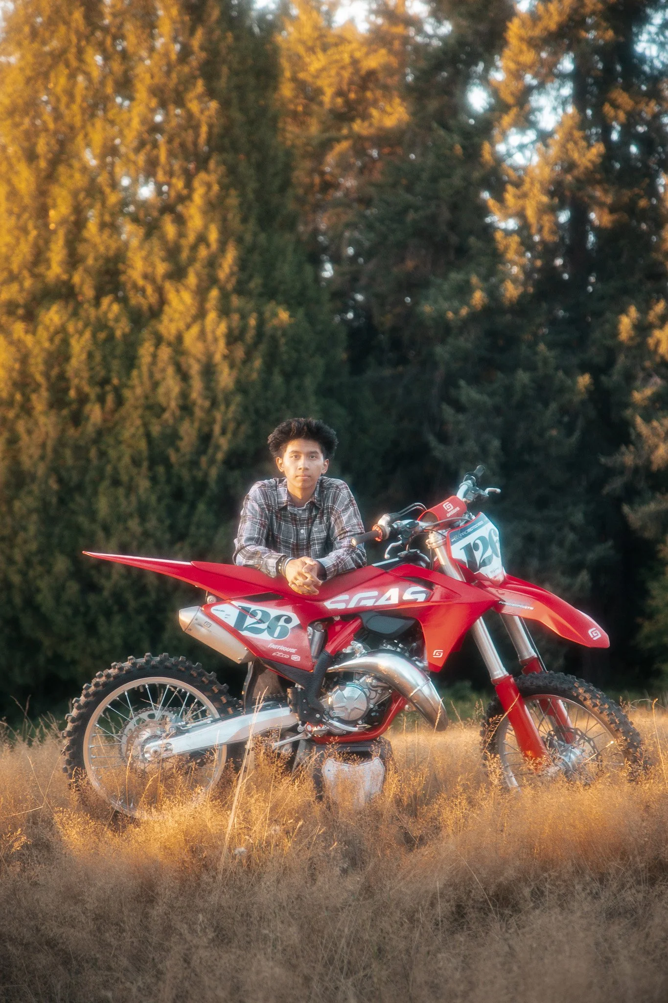 A person with a red dirt bike in a grassy field near trees.