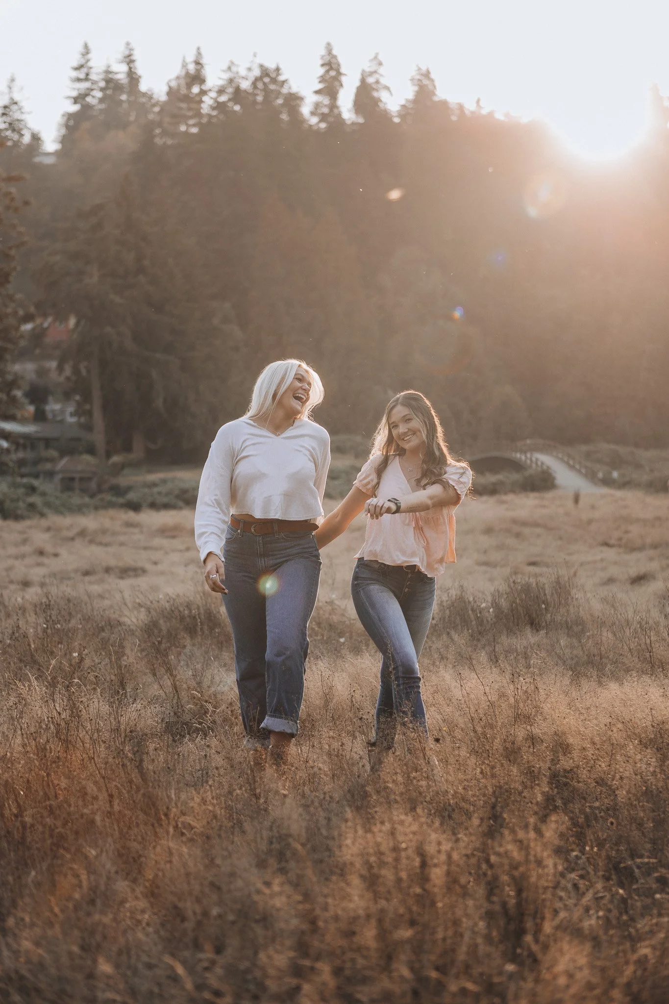 Two women smiling as they walk through a sunlit grassy field.