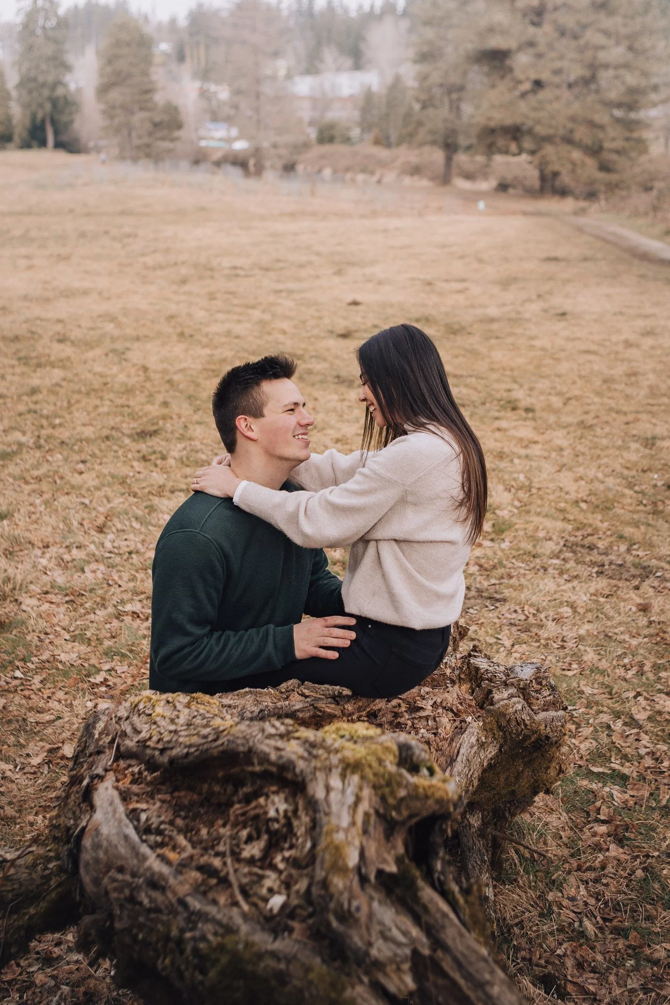 A smiling couple sitting together on a fallen tree in a park.