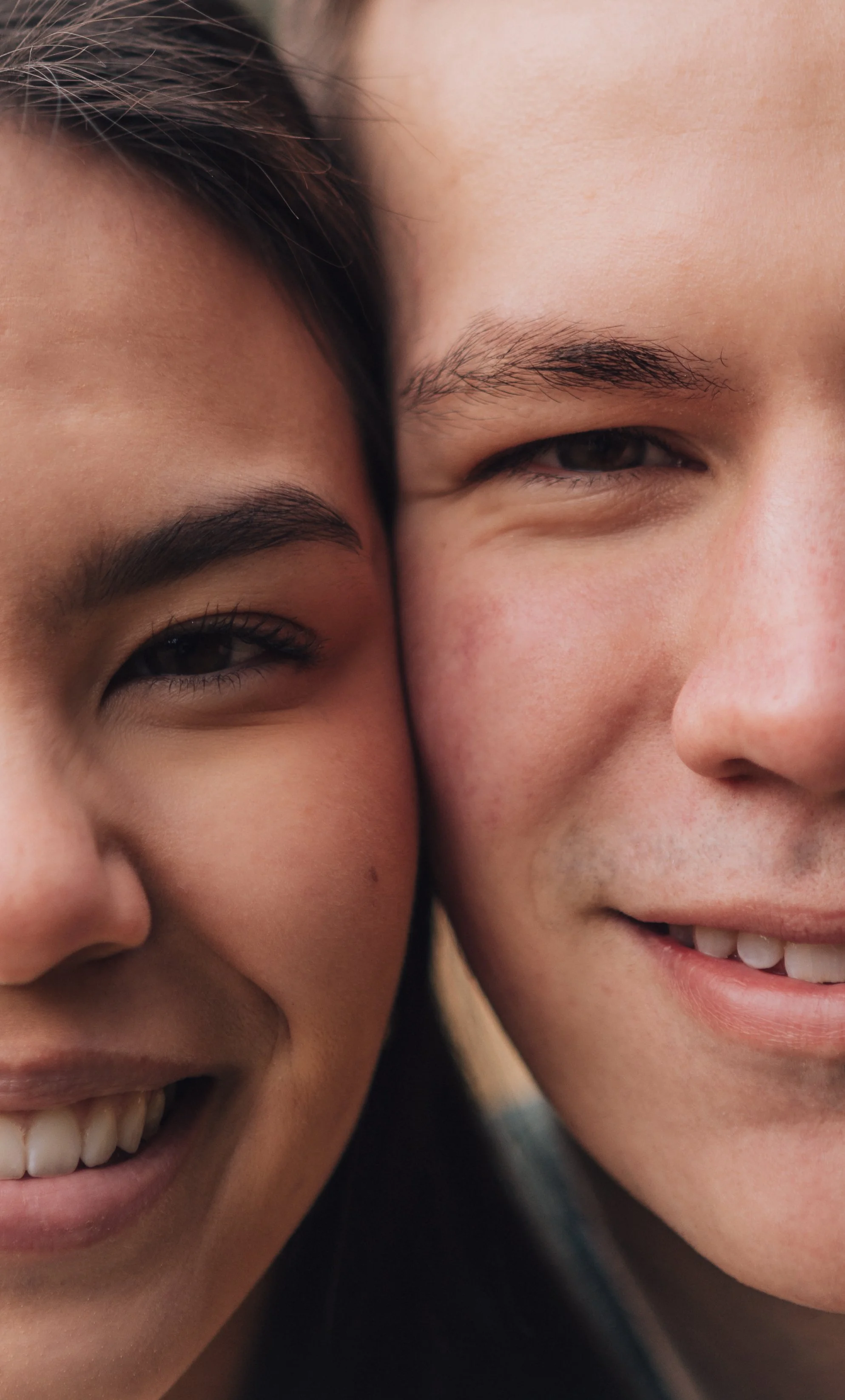 Close-up of two smiling people with their faces touching, showing their eyes, eyebrows, and partial smiles.