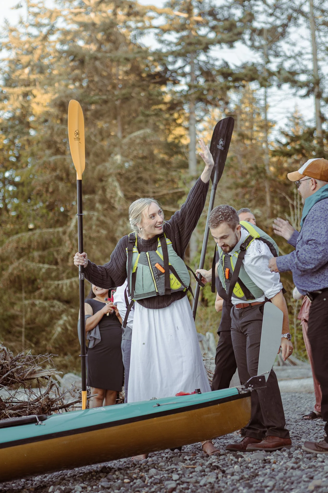 People with paddles and life jackets preparing to kayak beside a wooded shoreline.