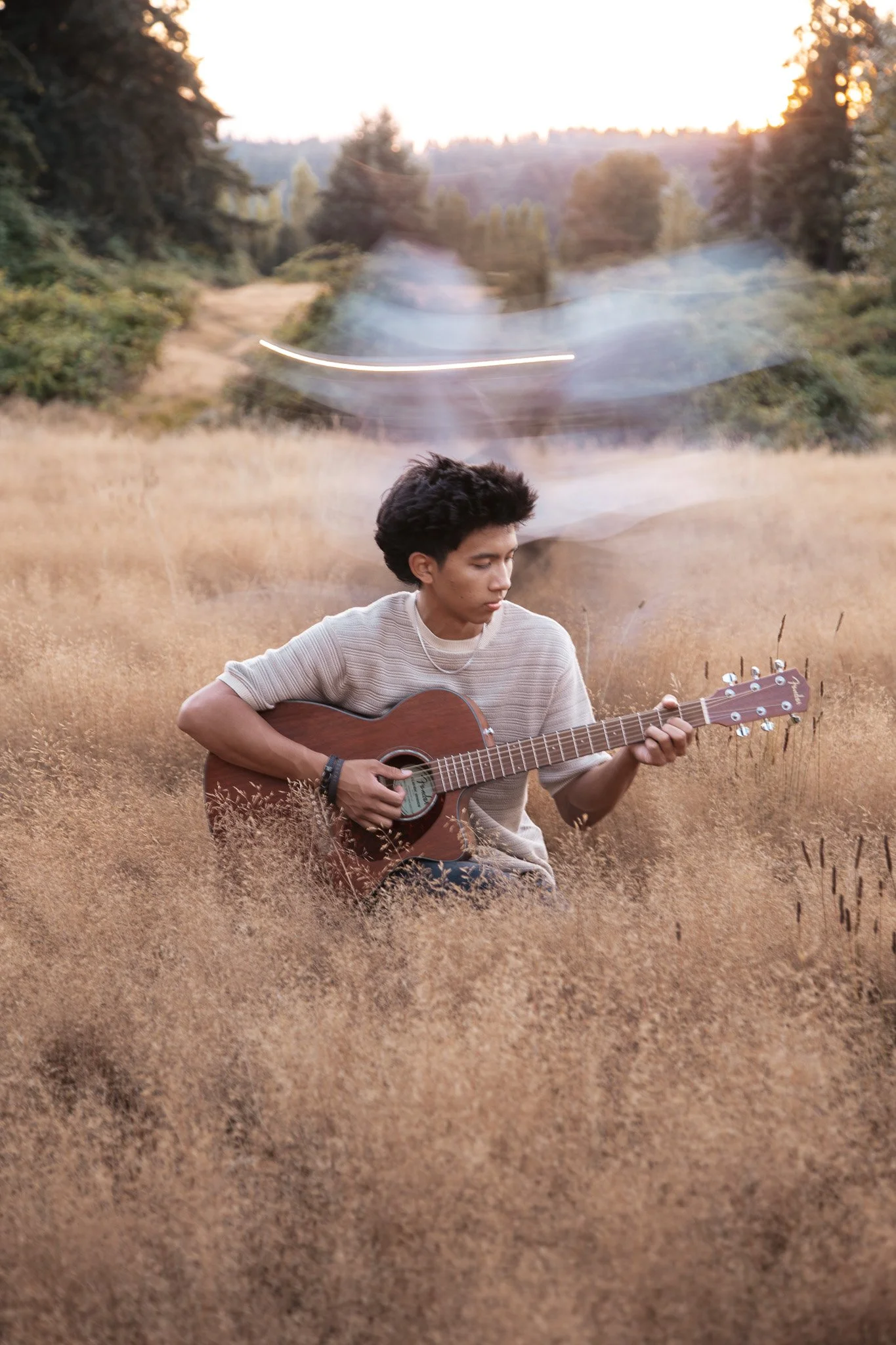 A man playing acoustic guitar in a field of golden grass.