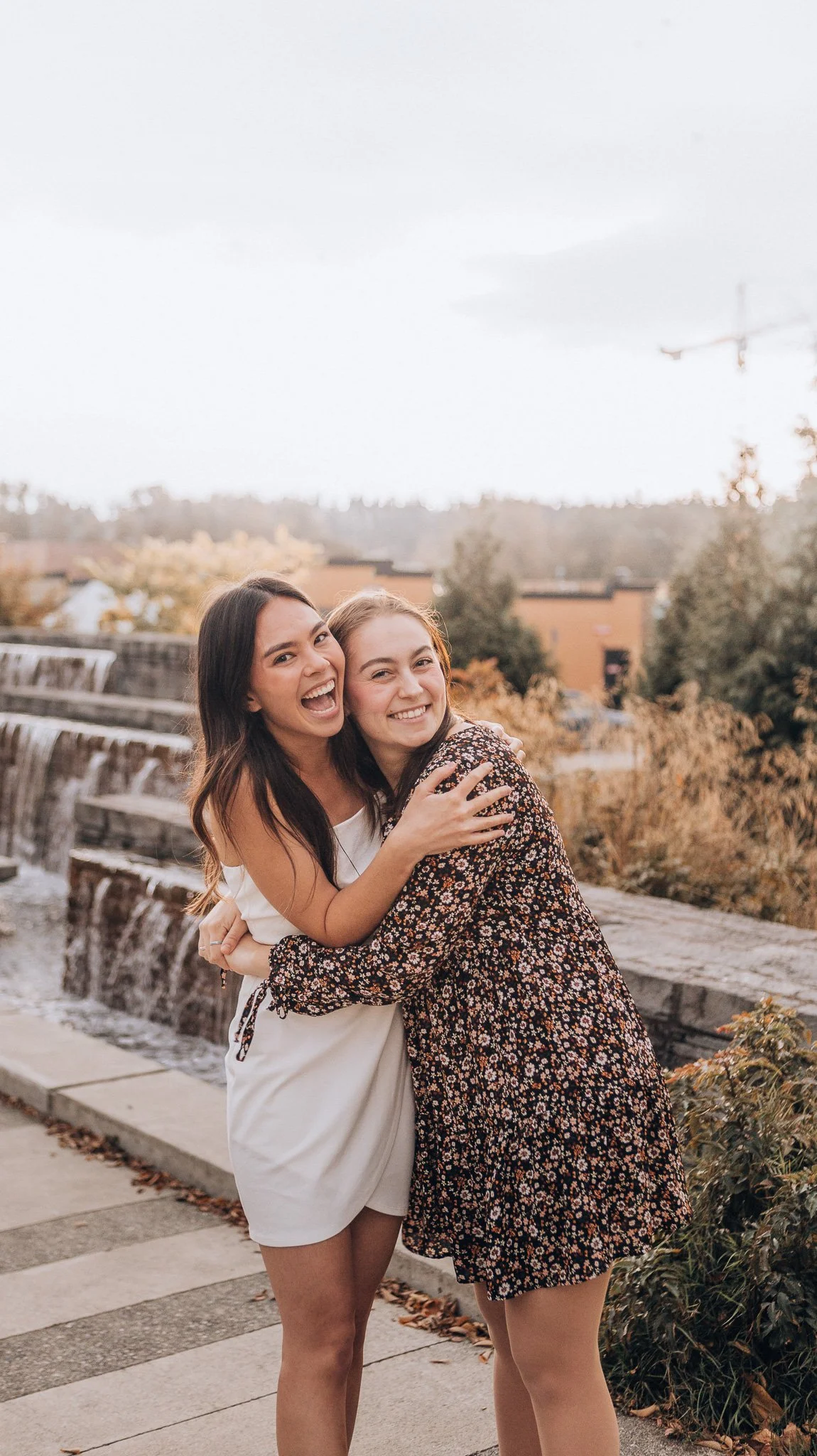 Two women embracing outdoors beside tall grasses.