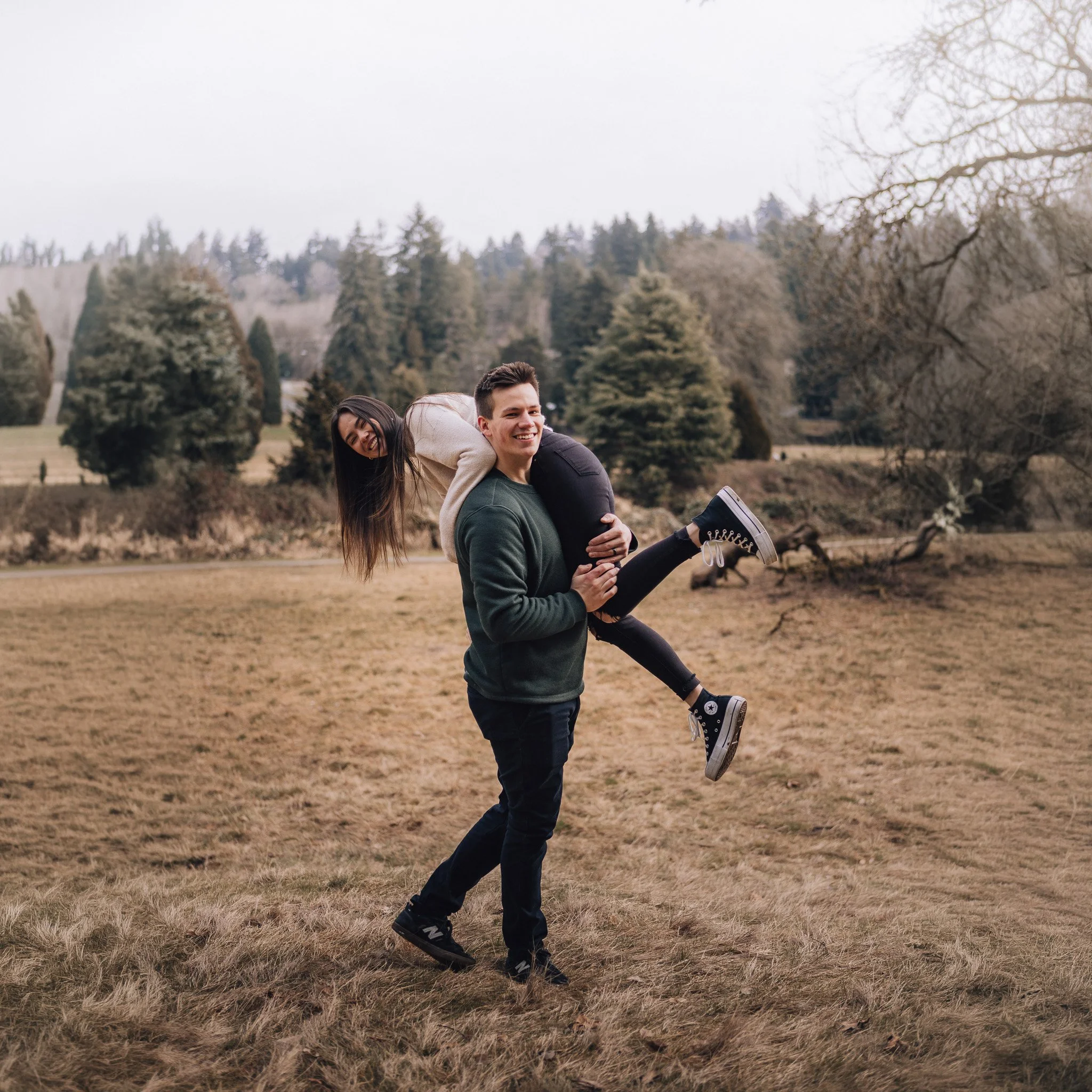 A smiling couple sharing a piggyback ride in a grassy park.