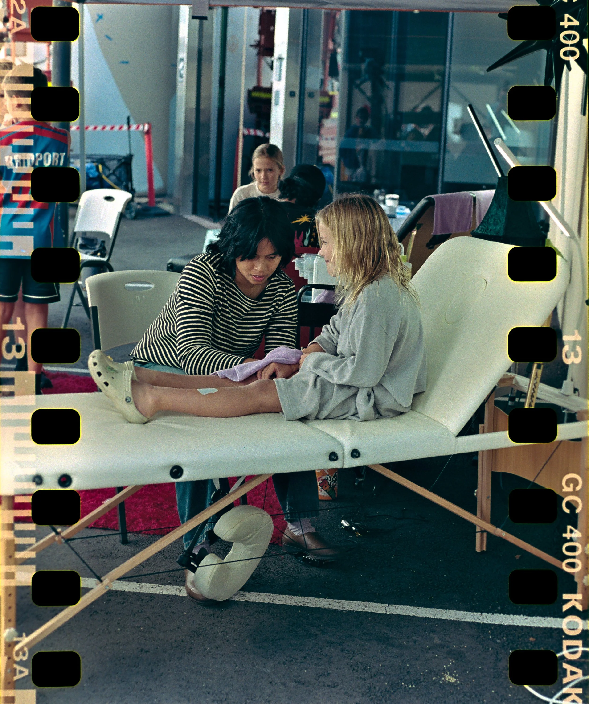 A young child sits on a tattoo bed and has a temporary tattoo applied by a performer.