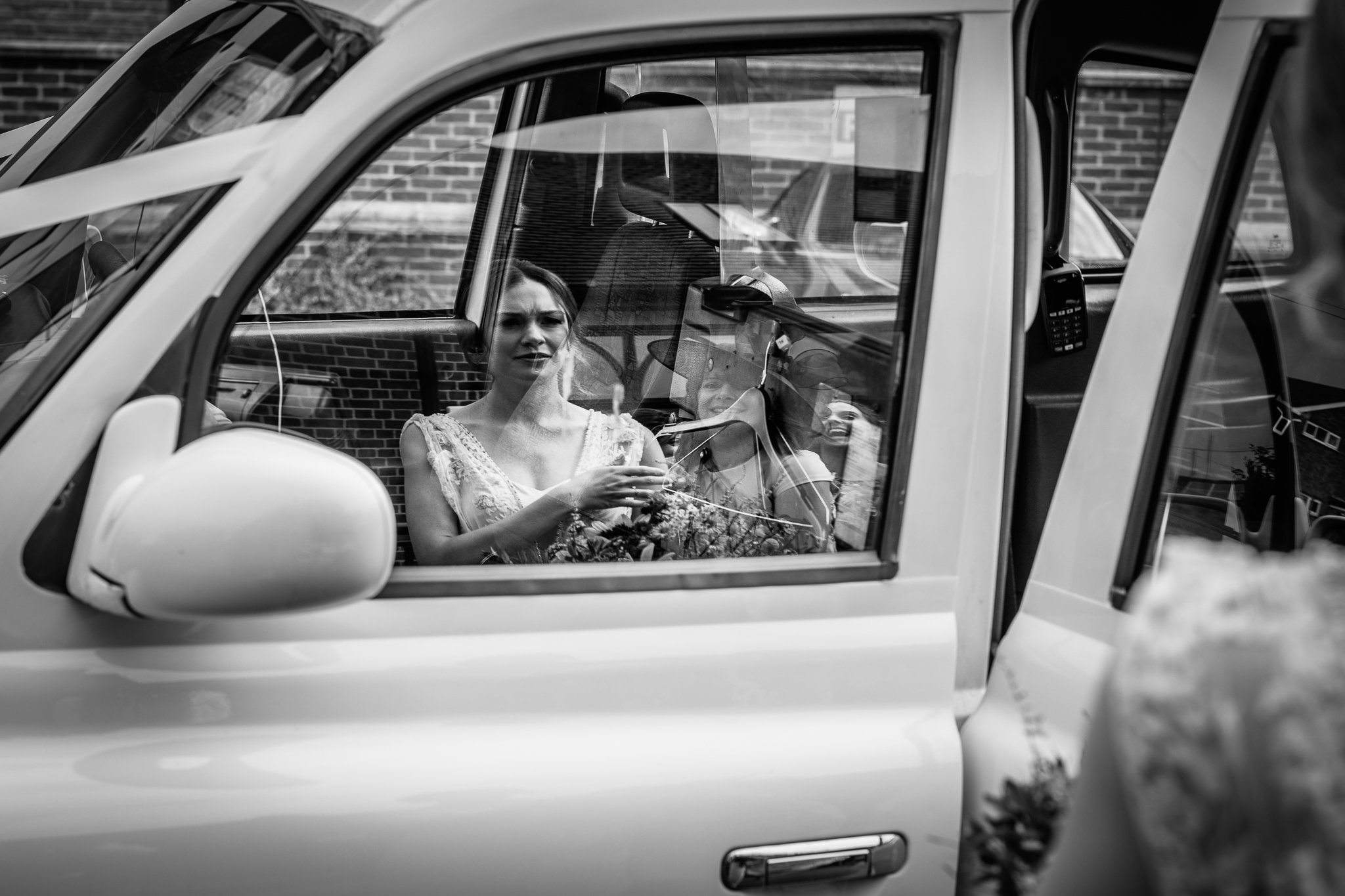  Bride looks at her reflection in a car window at The Holy Family Church in Reigate 