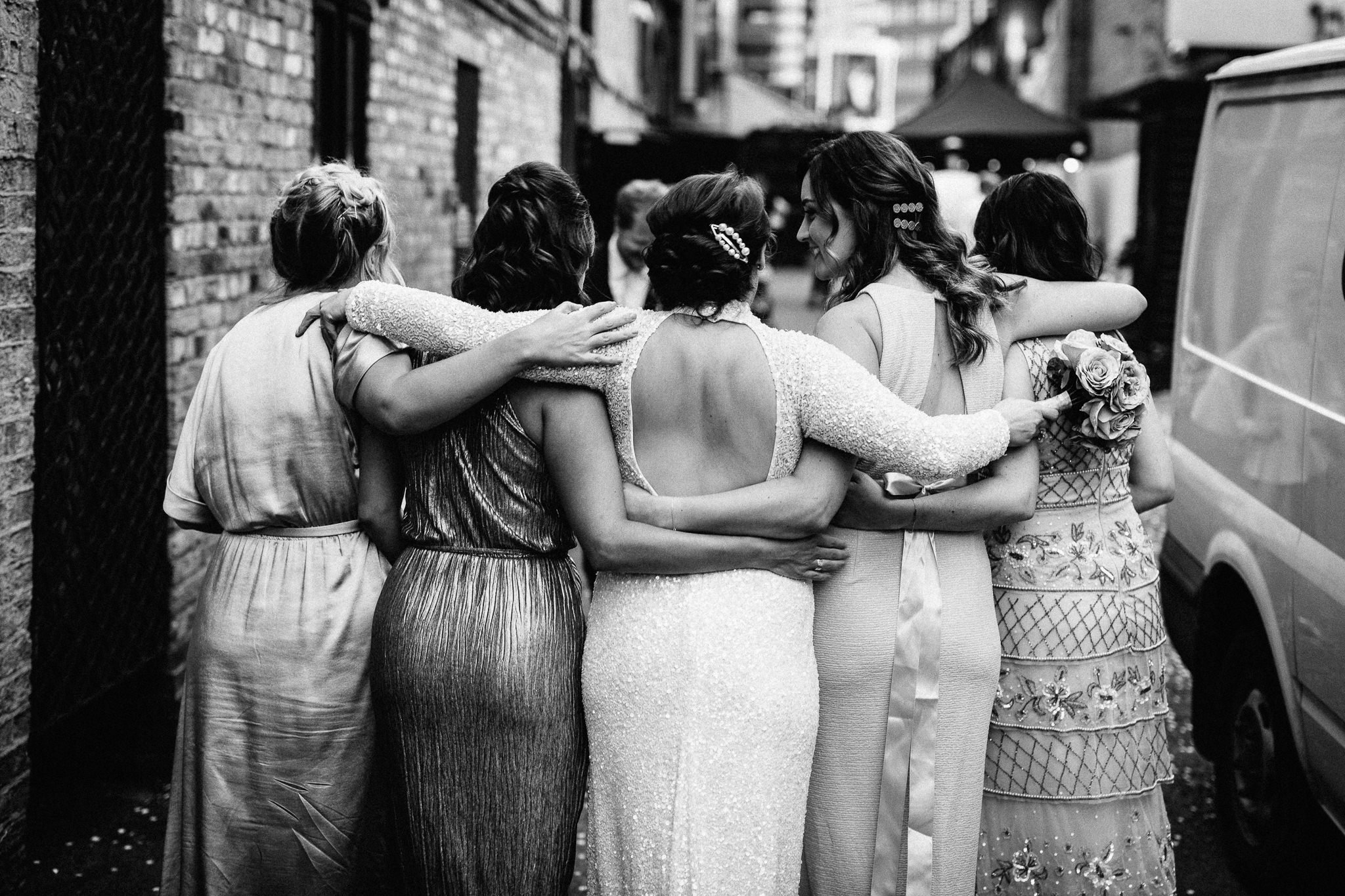  Bride and her bridesmaids with their arms around each other. 