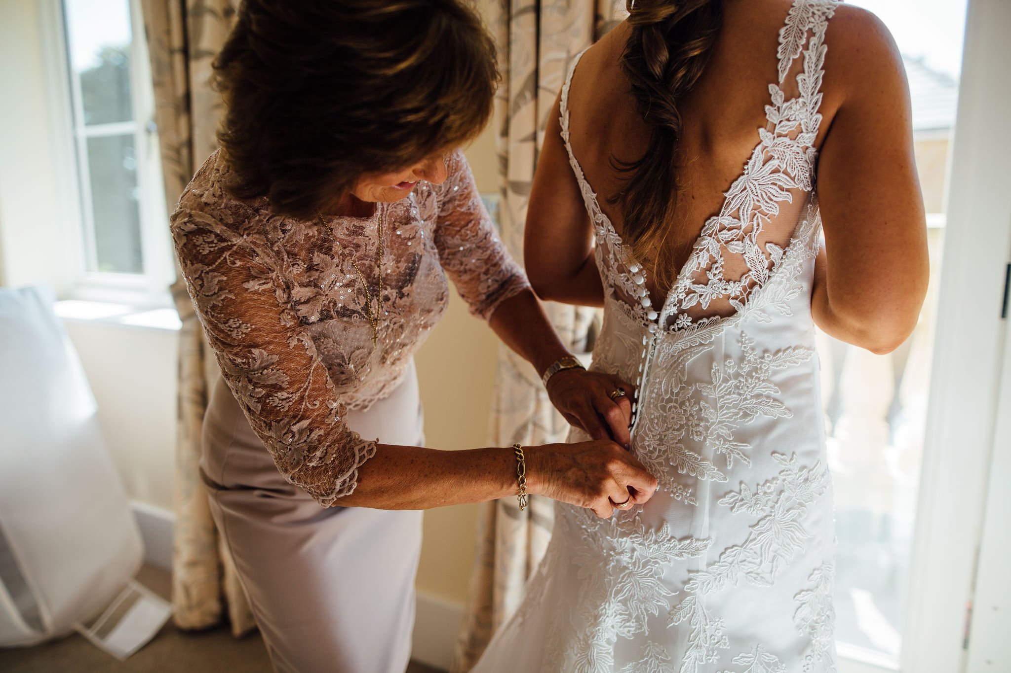  Mother of the Bride helps the Bride button up her dress on her wedding day 