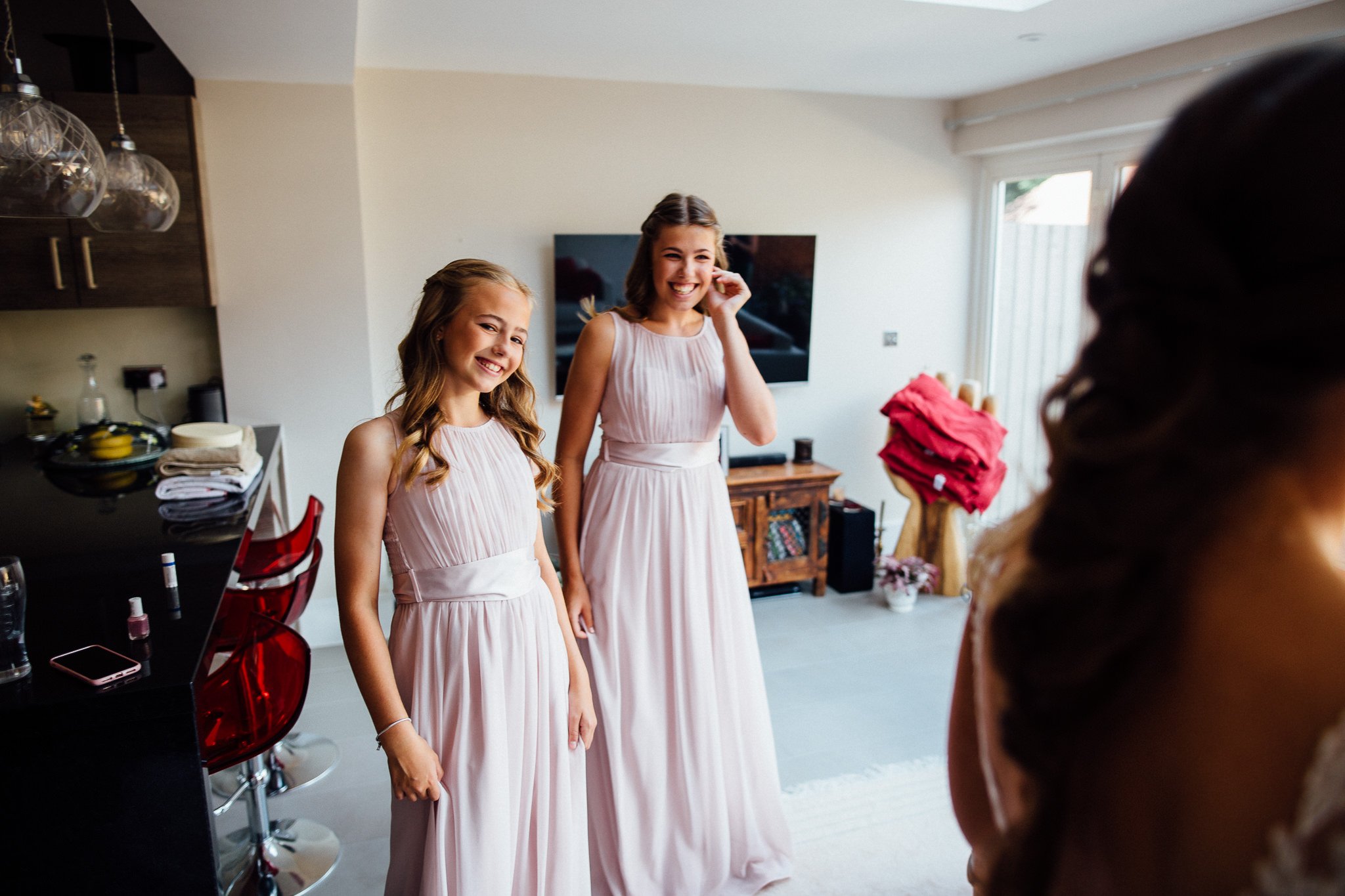  Bridesmaids smile at the bride at seeing her on her dress 