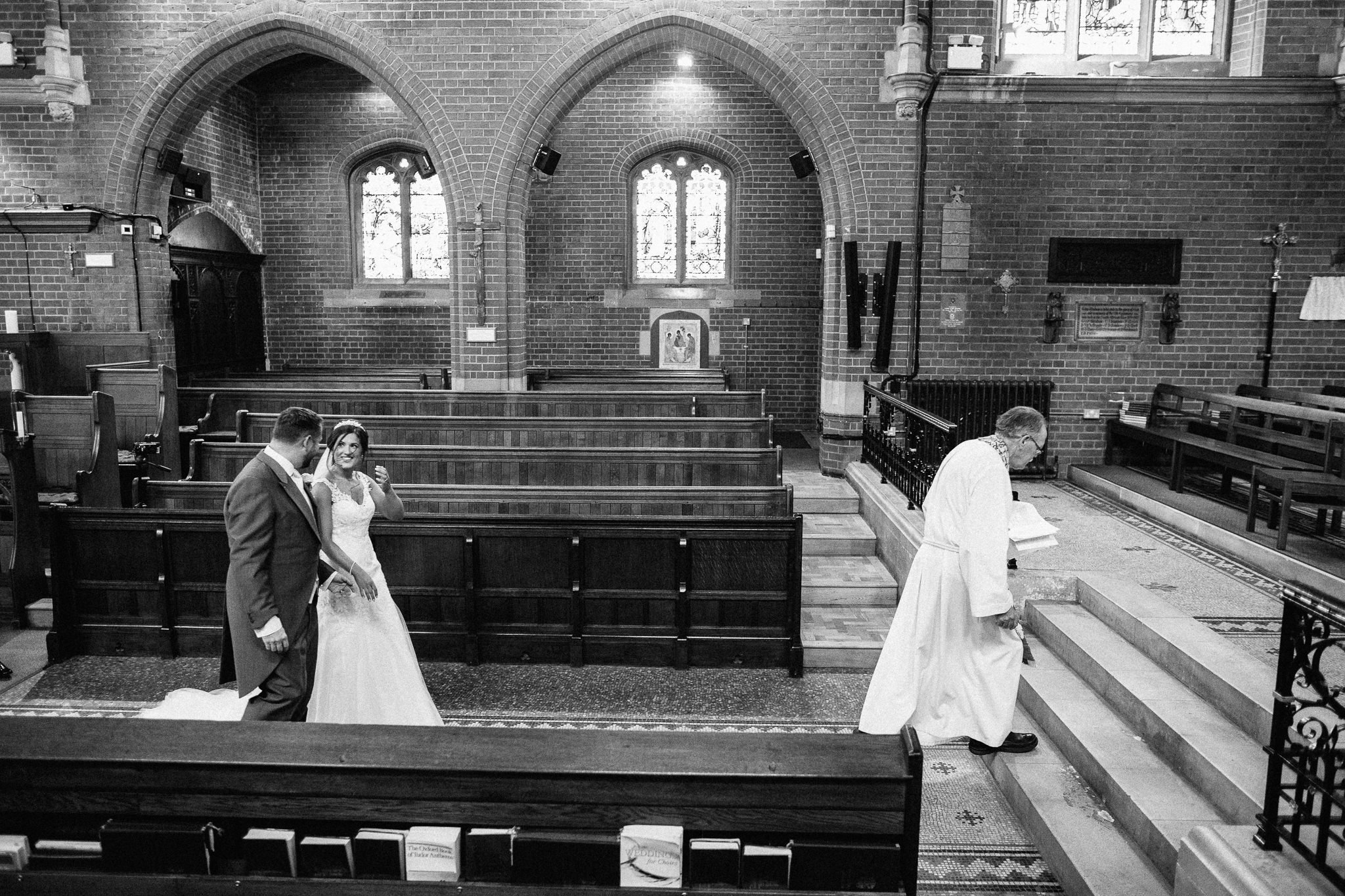  Bride and Groom follow the Vicar  at the Chapel of St Luke at Epsom College 