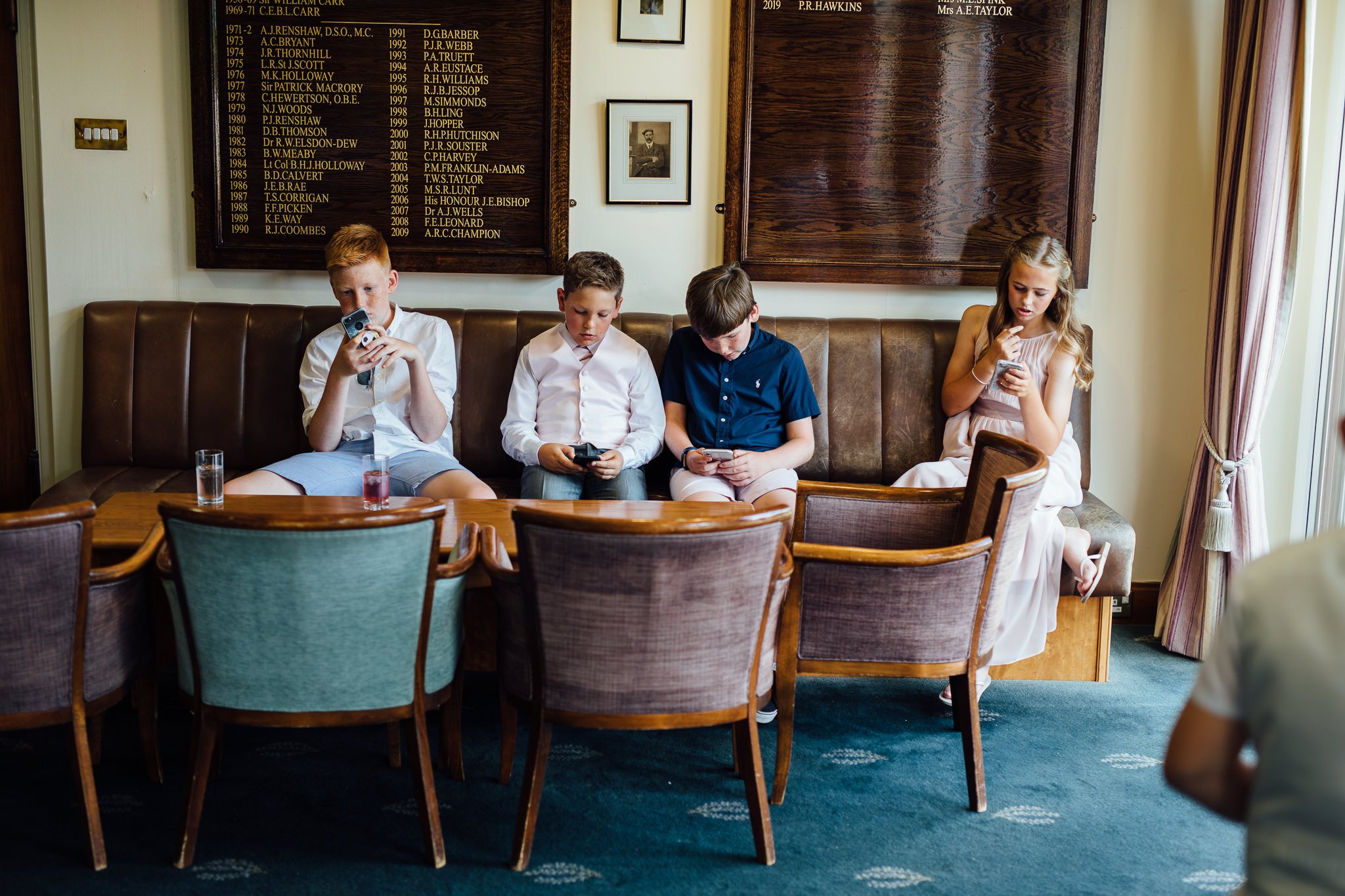  Young wedding guests stare at their phones  at Walton Heath Golf Club Surrey 