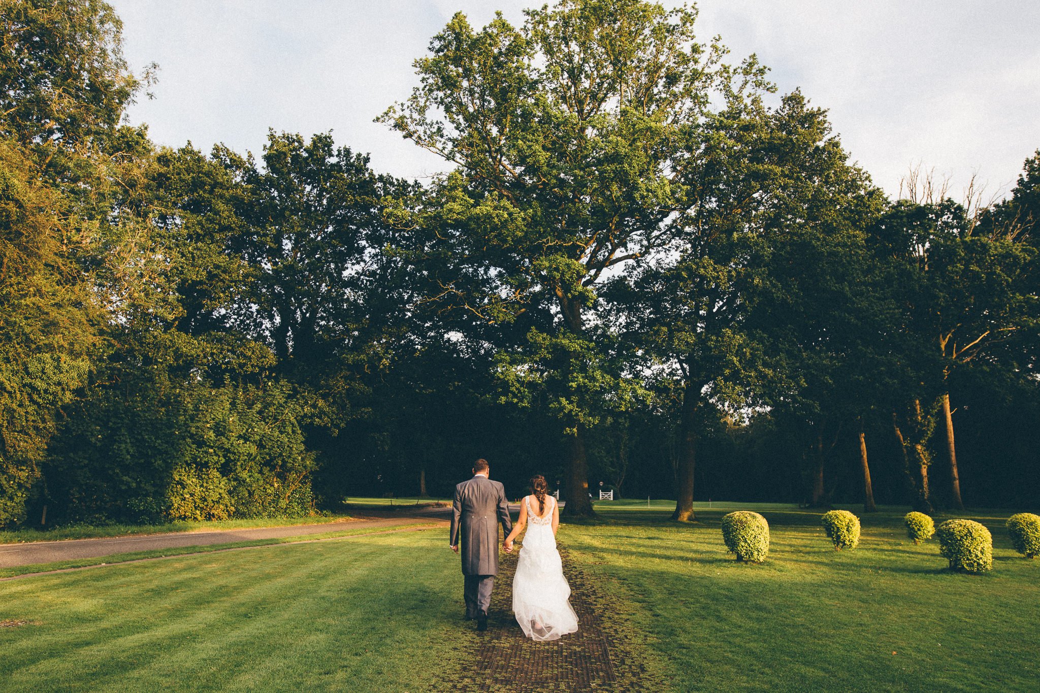  Bride and Groom walk hand in hand on the grounds of  at Walton Heath Golf Club Surrey 