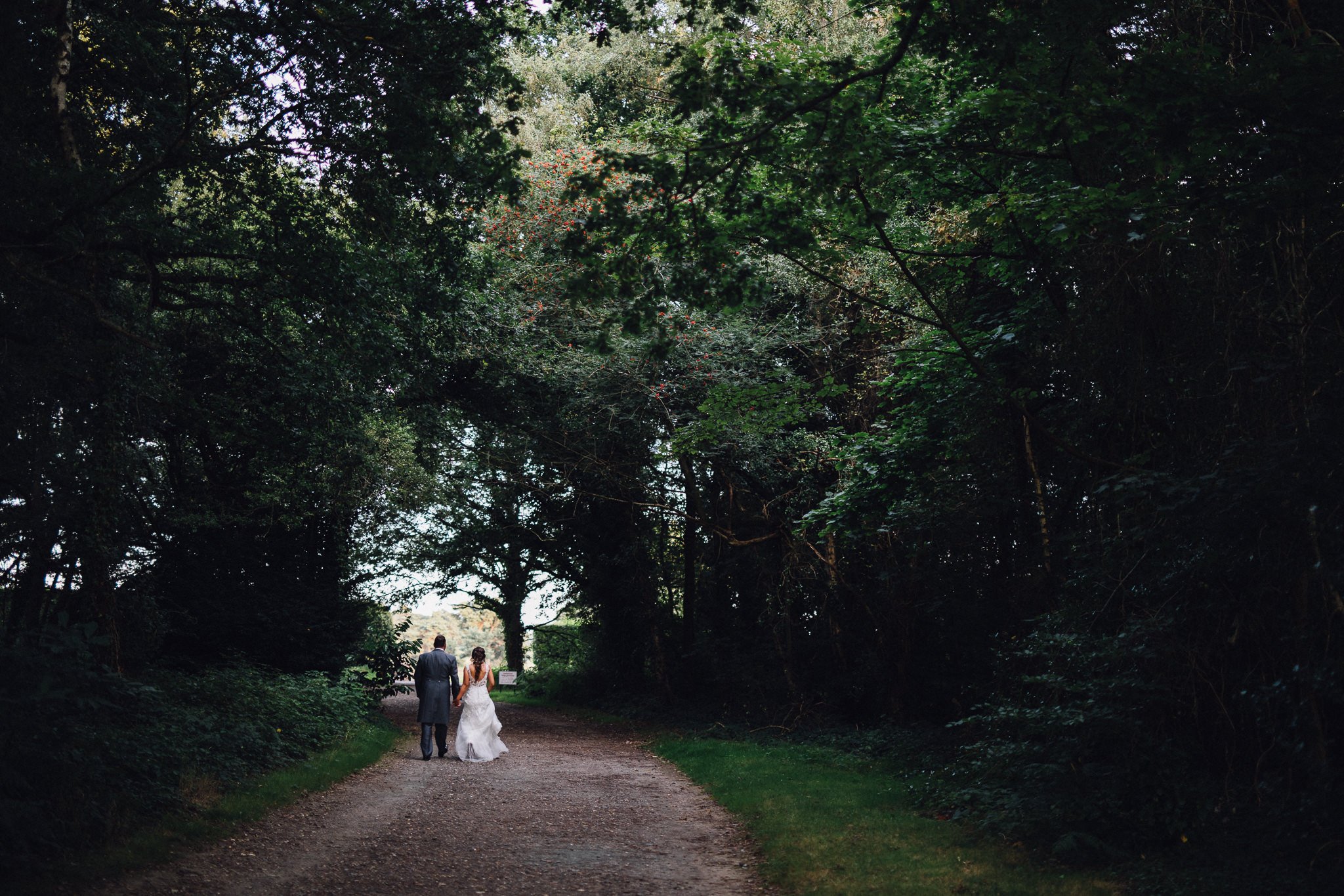  Bride and Groom walk through a wooded area on their wedding day  at Walton Heath Golf Club Surrey 
