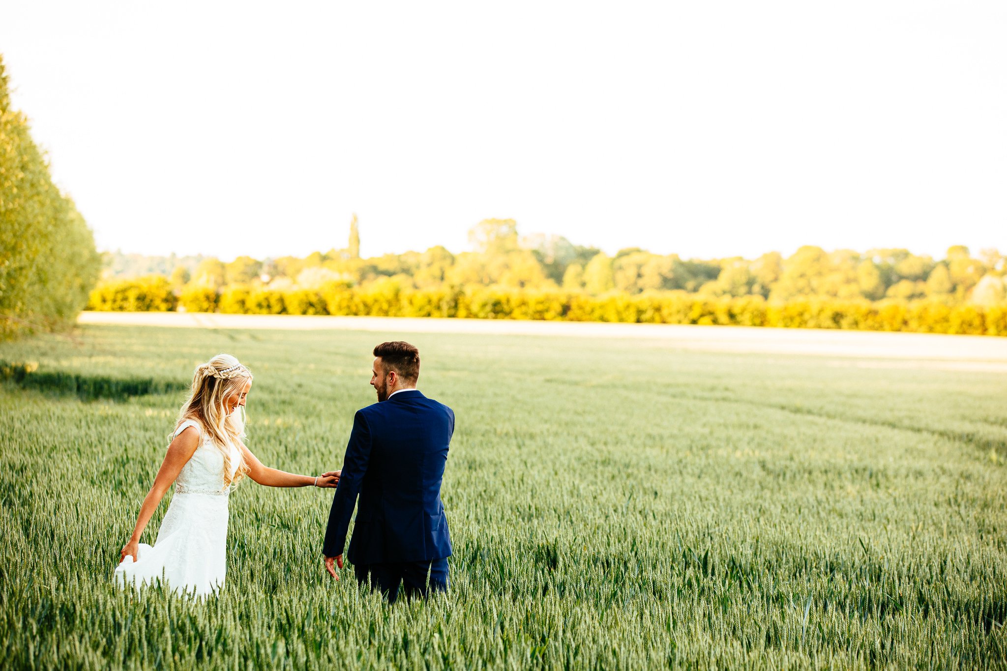  Groom leads the Bride through a field at Winters Barns Wedding Venue Kent 