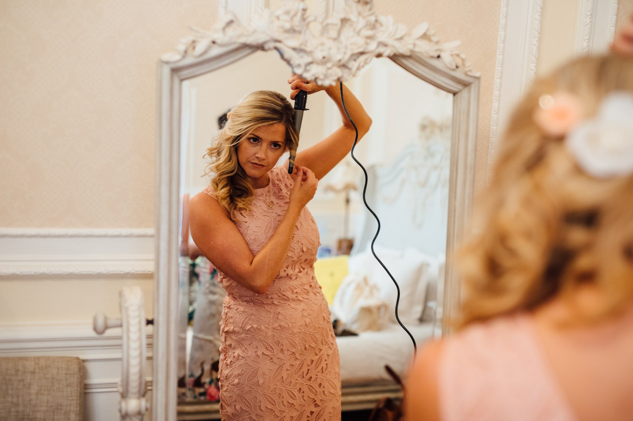  Bridesmaid curling her hair whilst looking in the mirror 