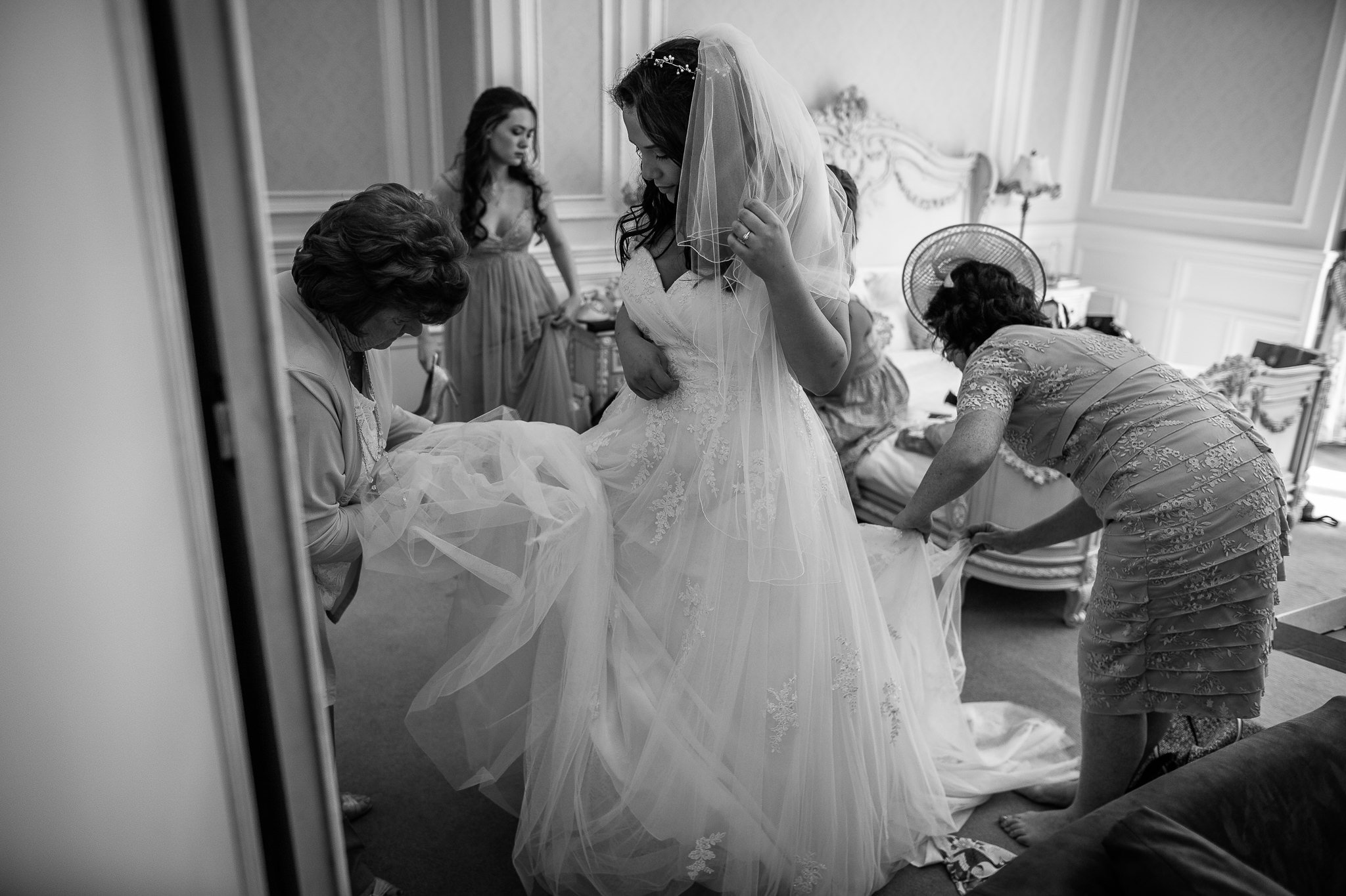  Bride in her wedding dress as her Bridal party help with the final adjustments at Warren House Hotel Kingston upon Thames 