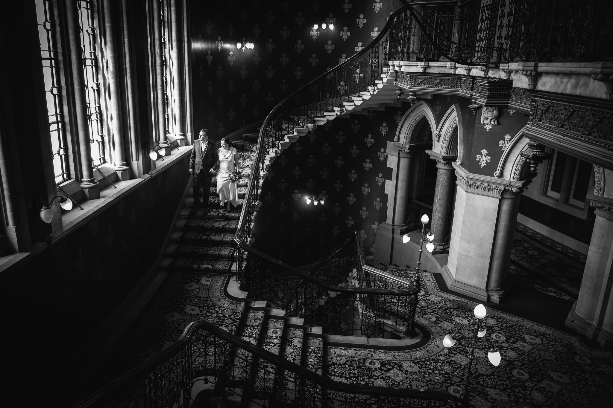  Bride and Groom descend the staircase as light comes in through the window at St. Pancras Renaissance Hotel London 