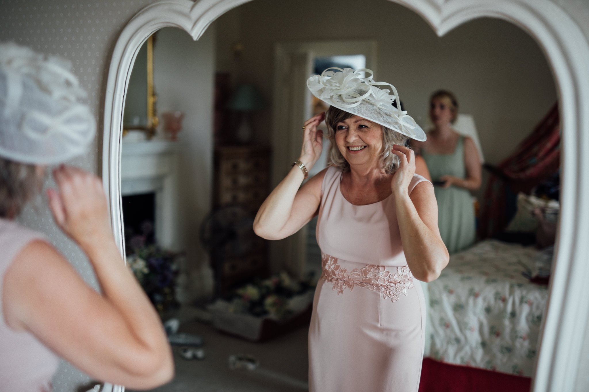  Mother of the bride adjusts her wedding hat in the mirror at  Wadhurst castle wedding venue 