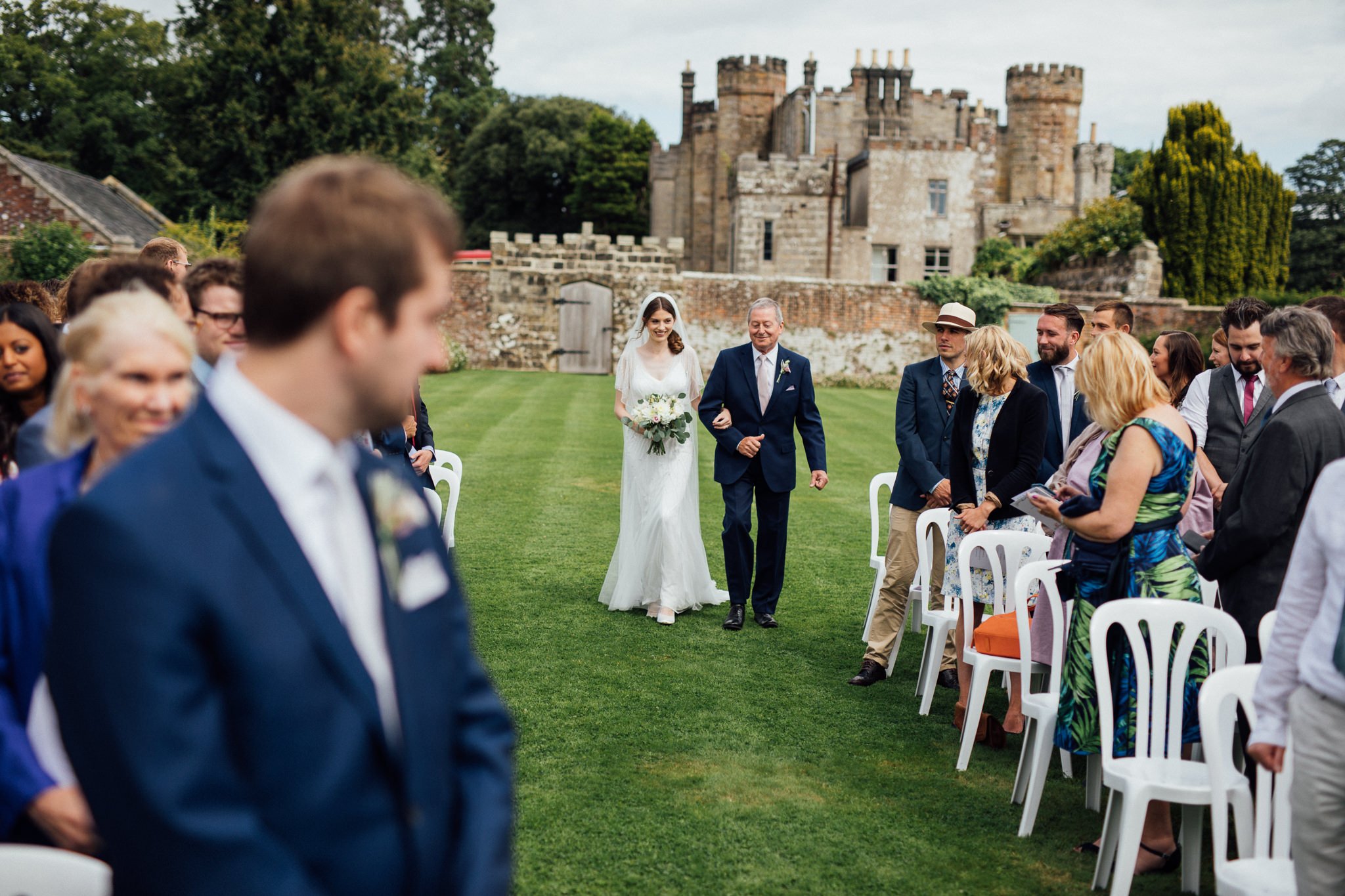  Bride and father of the bride walk down the aisle  in the walled garden at  Wadhurst castle wedding venue 