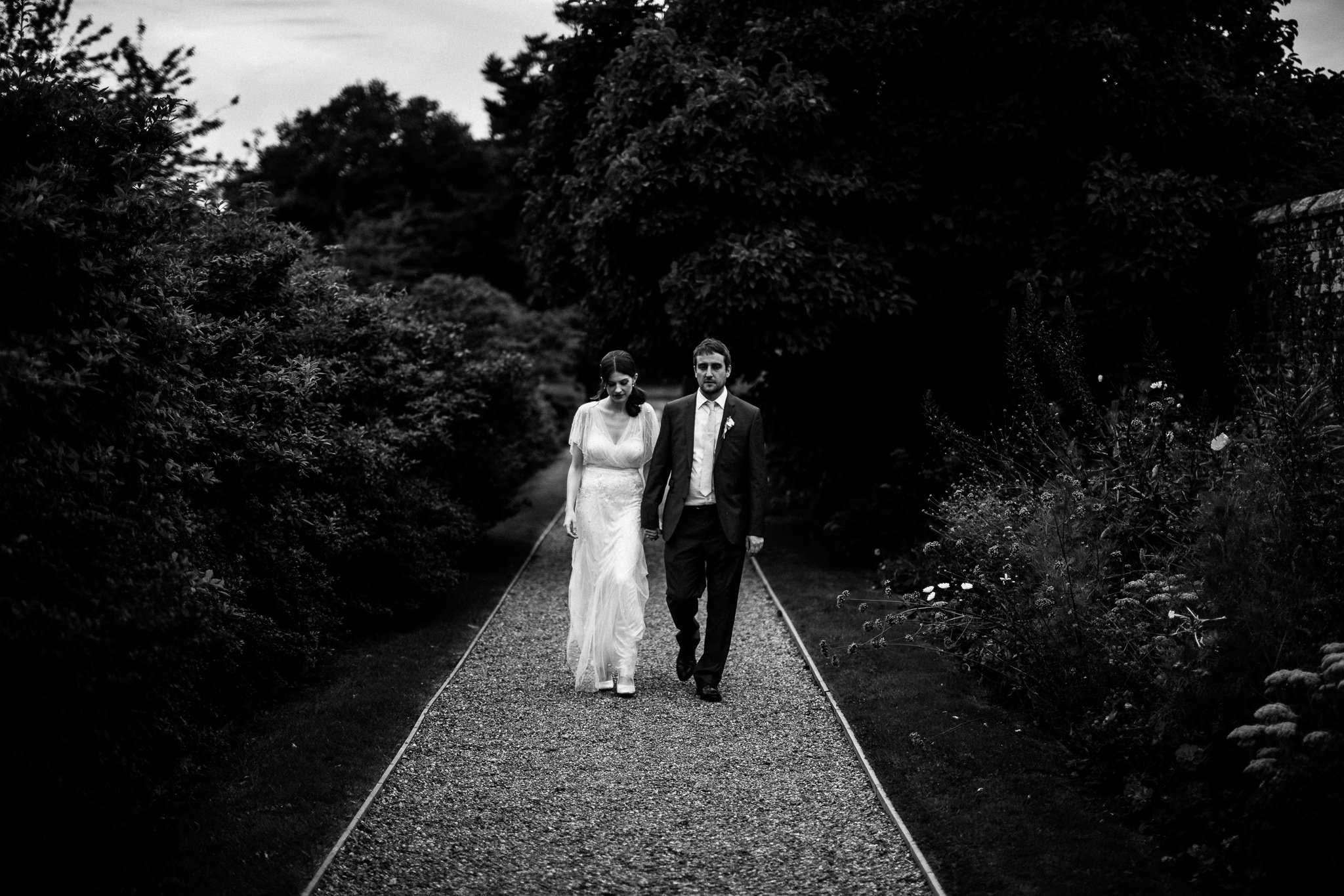  Bride and Groom walk along a gravel path at  Wadhurst castle wedding venue 