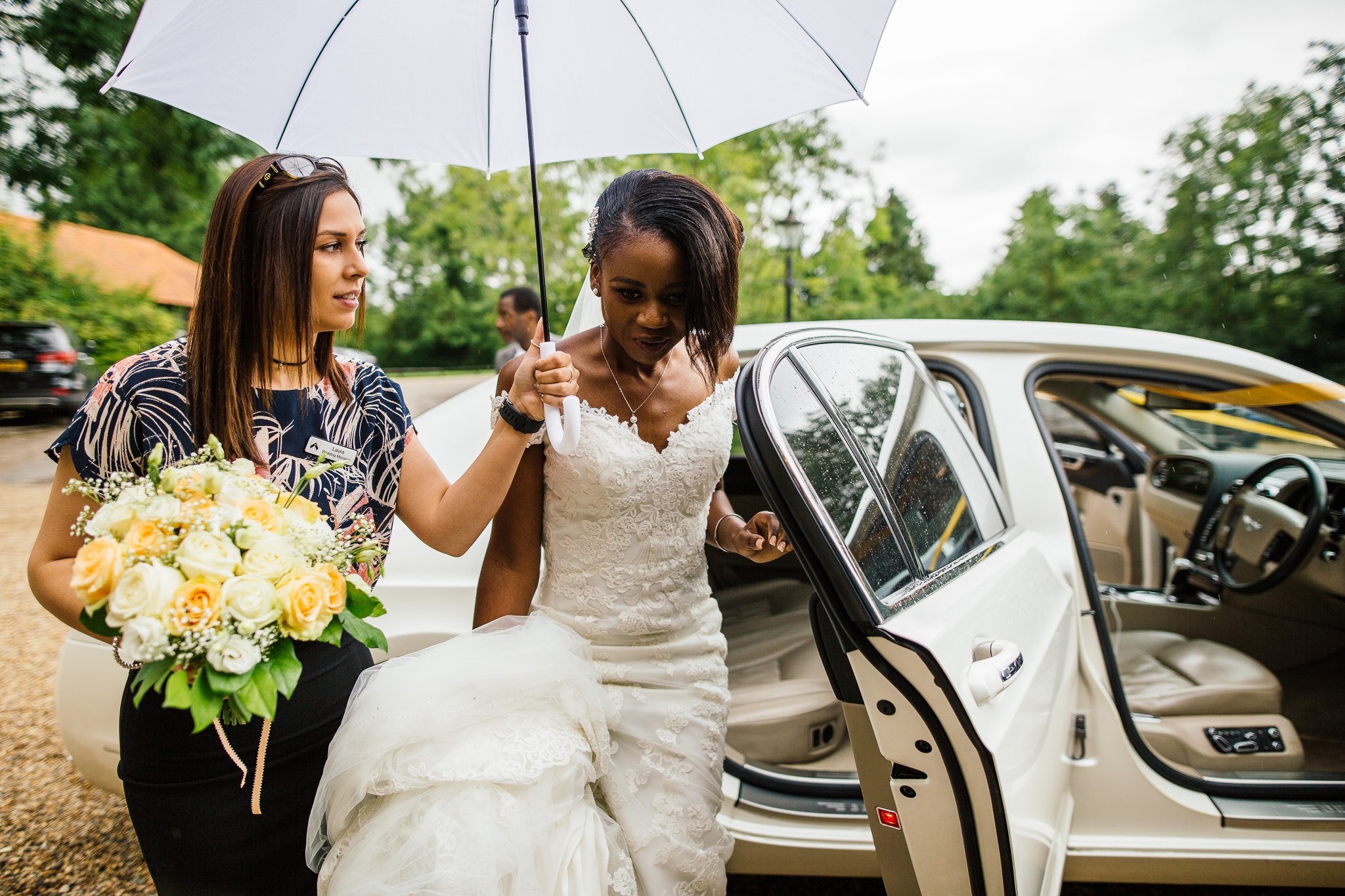  Bride getting out of car under an umbrella at Newland Hall Essex 