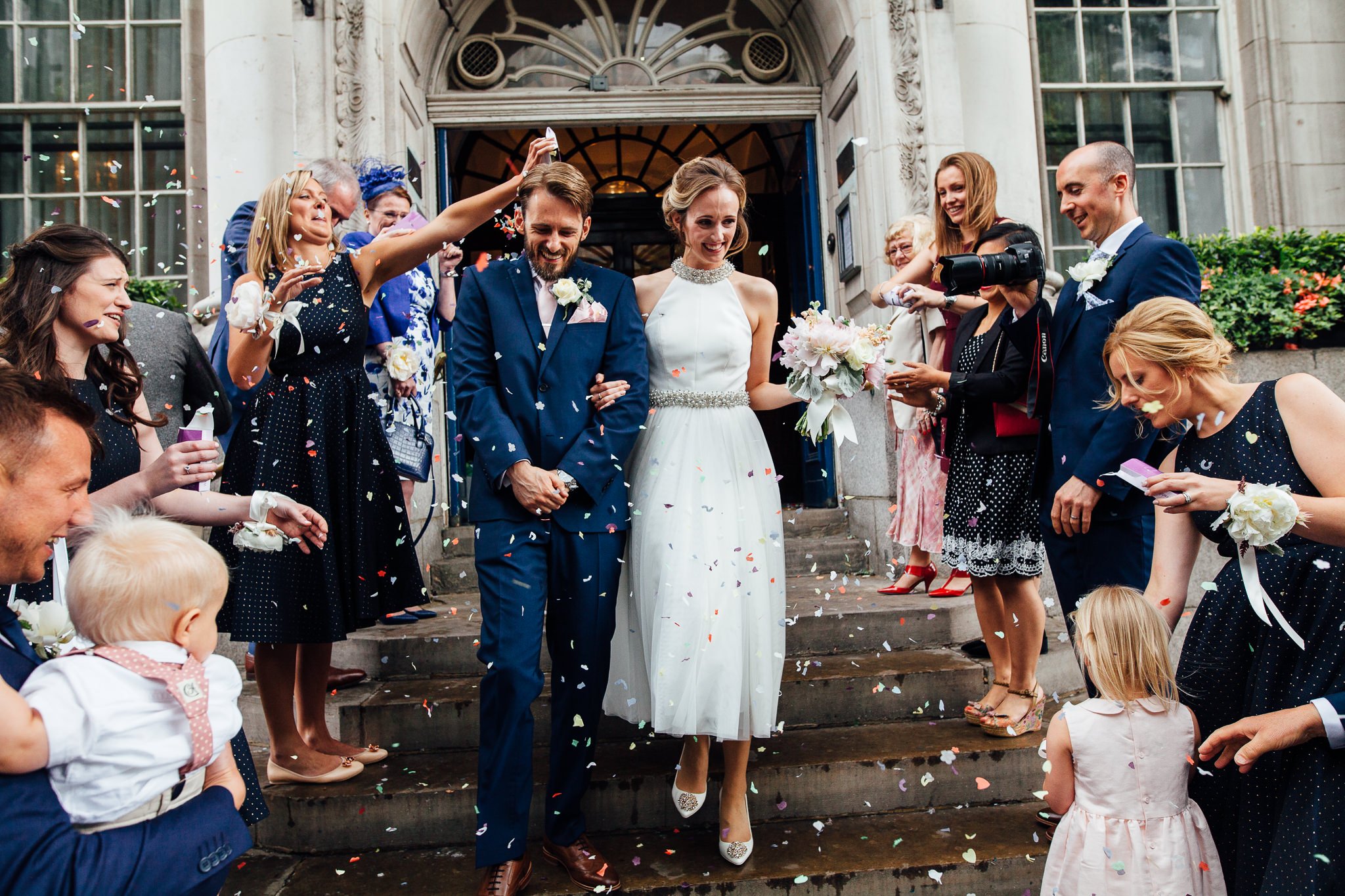  Bride and Groom walk down the steps at Chelsea Old Town Hall as they have confetti thrown at them 