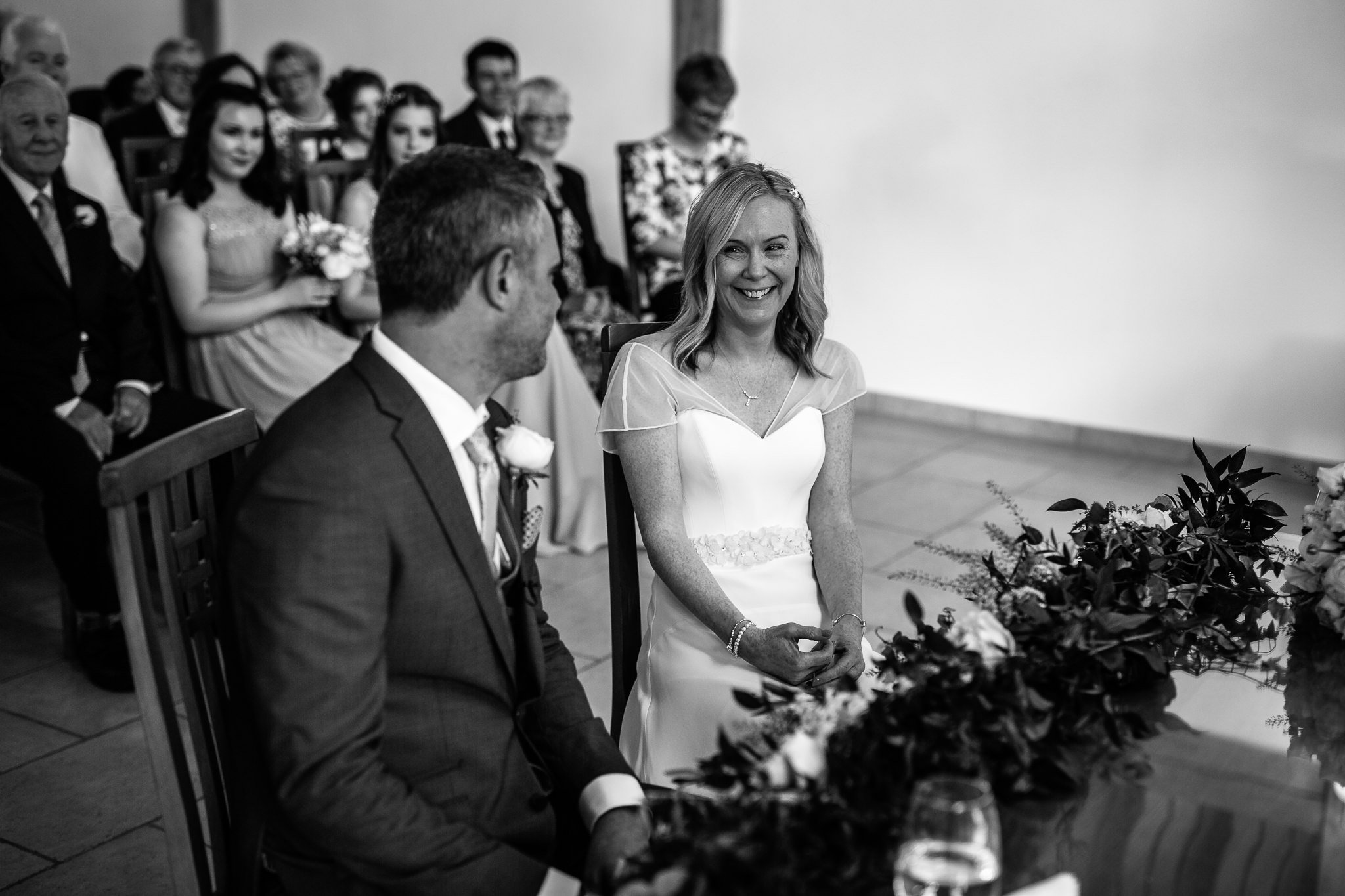  Bride smiling as she sits next to the groom in the ceremony room at Rivervale Barn 