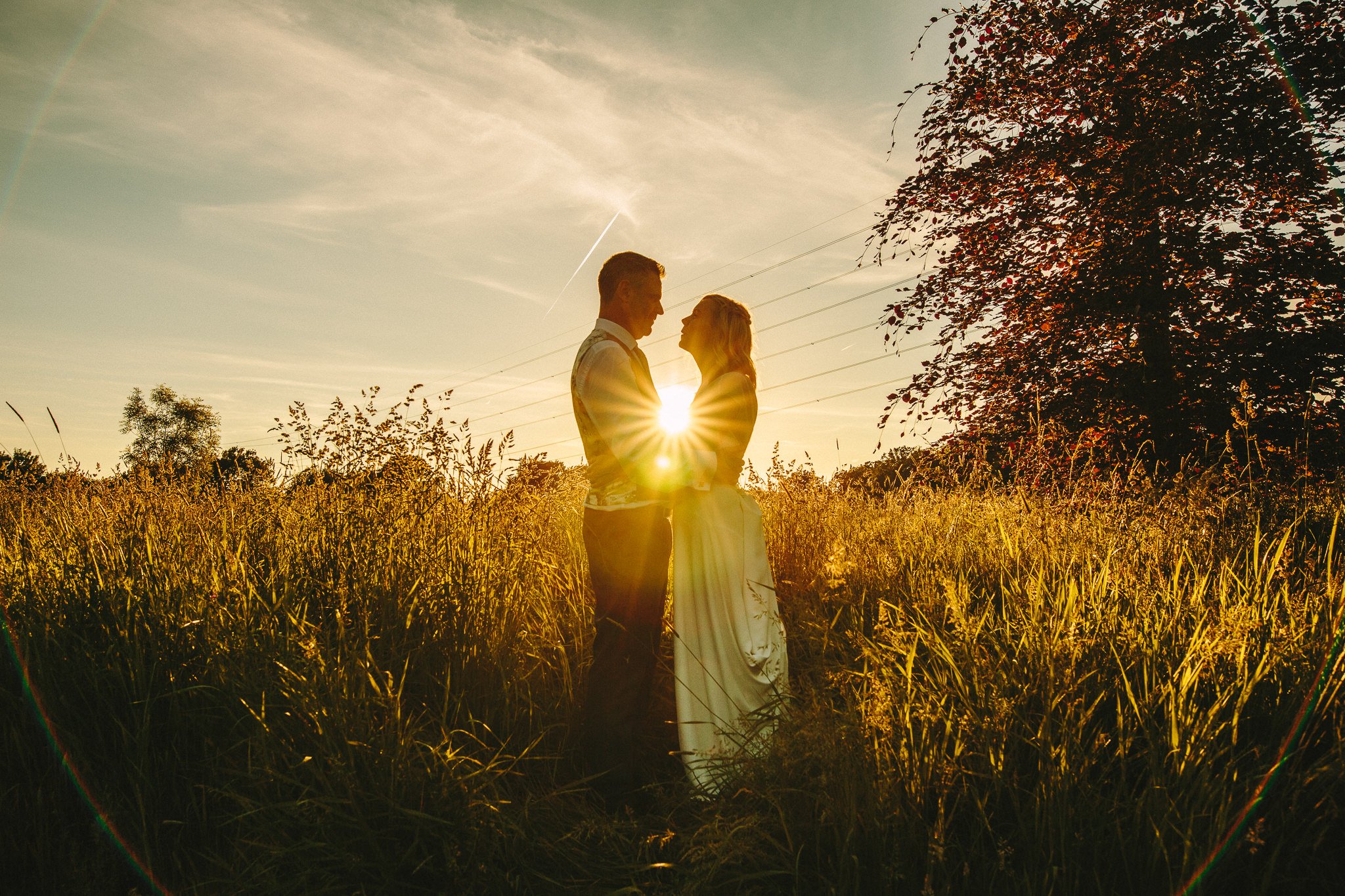  Bride and Groom standing in a field as the sun shines behind them at Rivervale Barn 