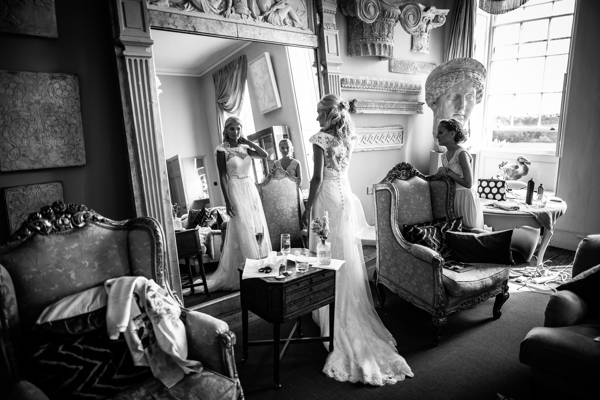  Bride in her wedding dress looking in a large full length mirror at Aynhoe Park 