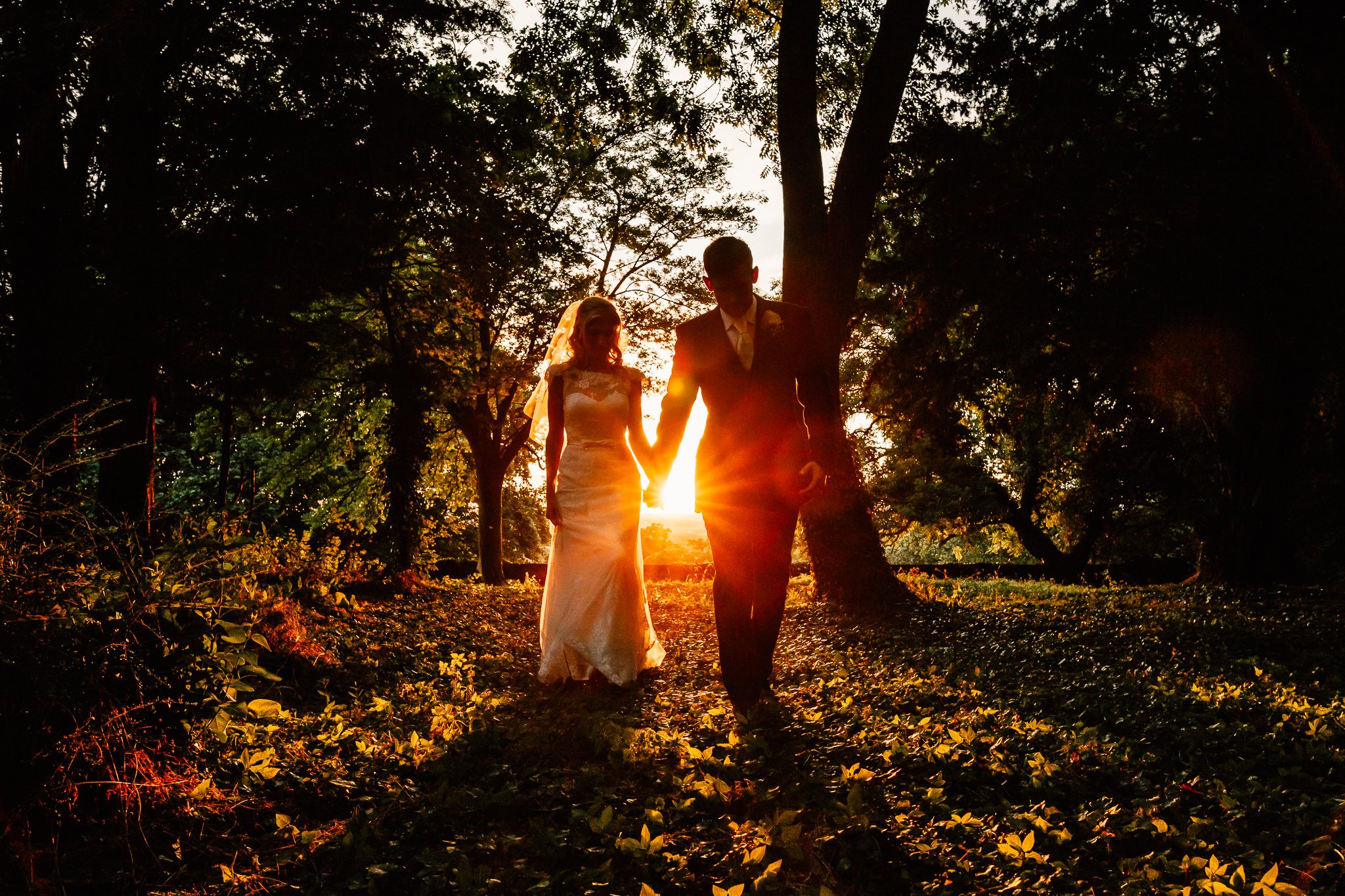  Bride and Groom hold hands as they walk through a wooded area at Aynhoe Park 