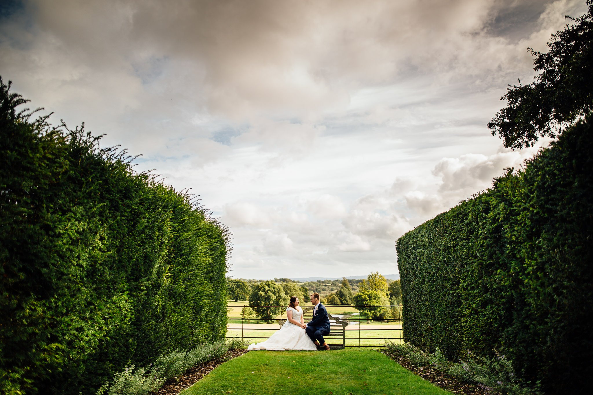  Bride and Groom sit on a bench in the garden at Wadhurst Castle 