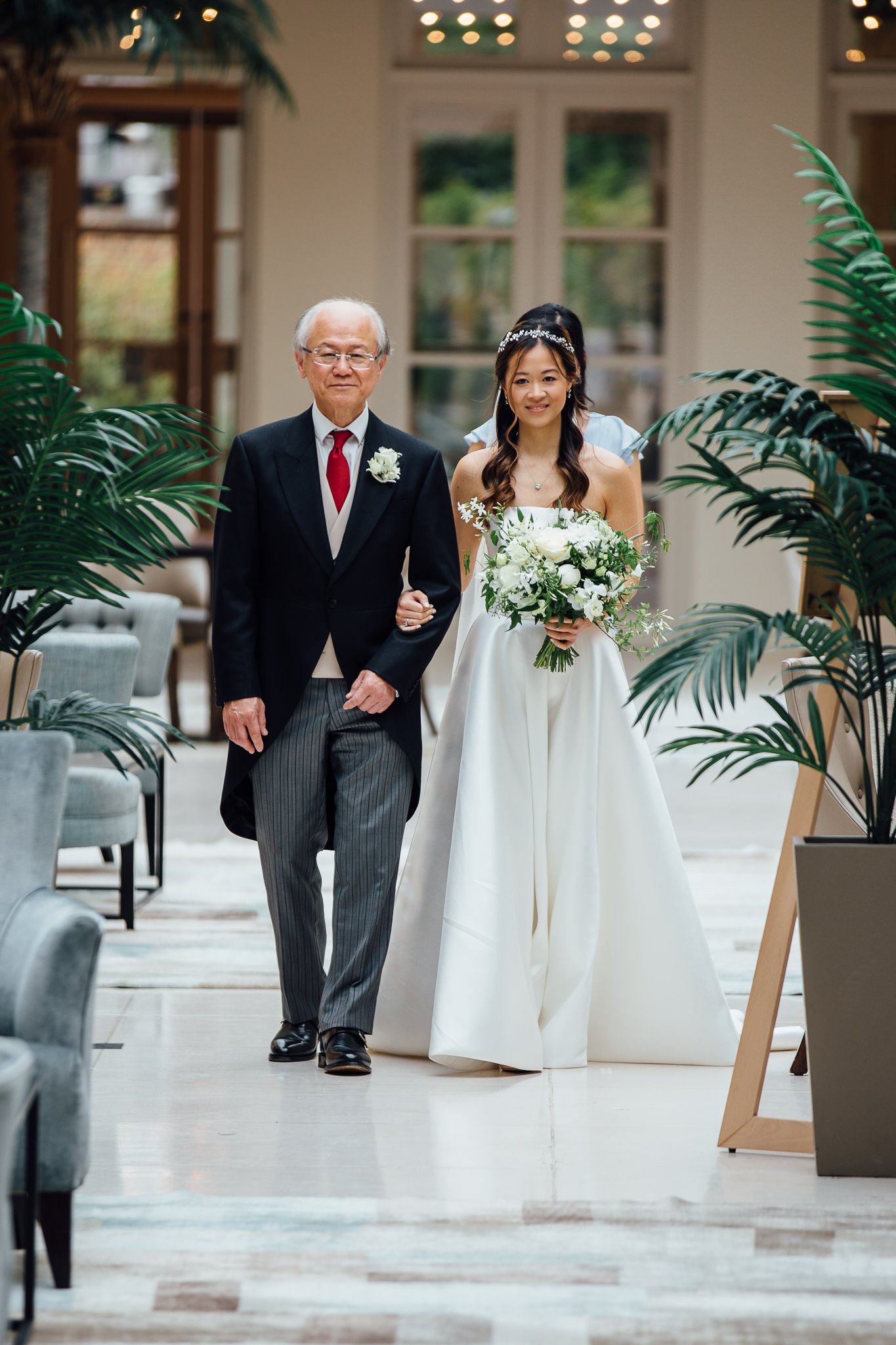  Bride walks down the aisle with her father during the wedding ceremony at The Hurlingham Club  