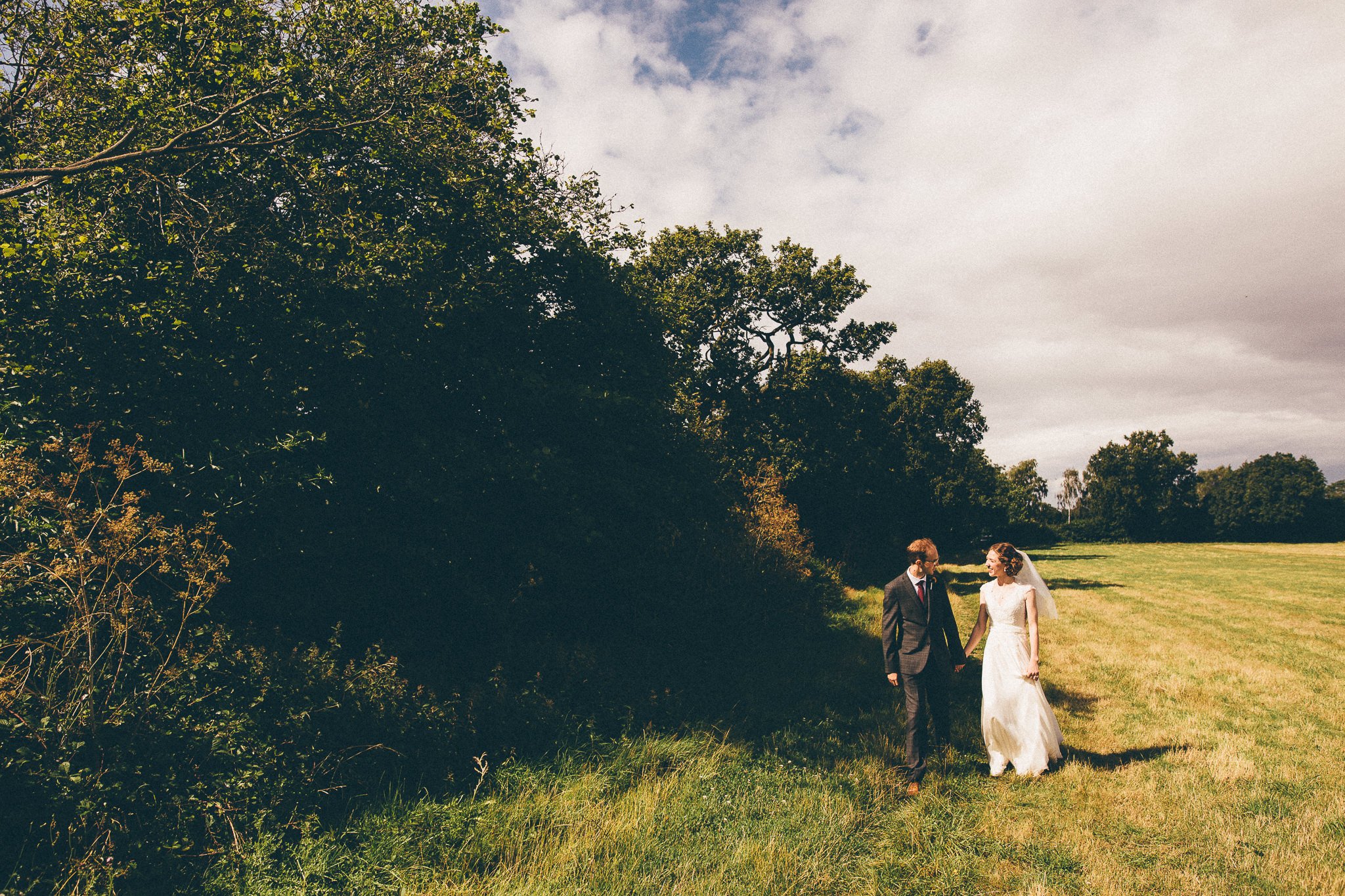  Bride and Groom walk hand in hand in a field 