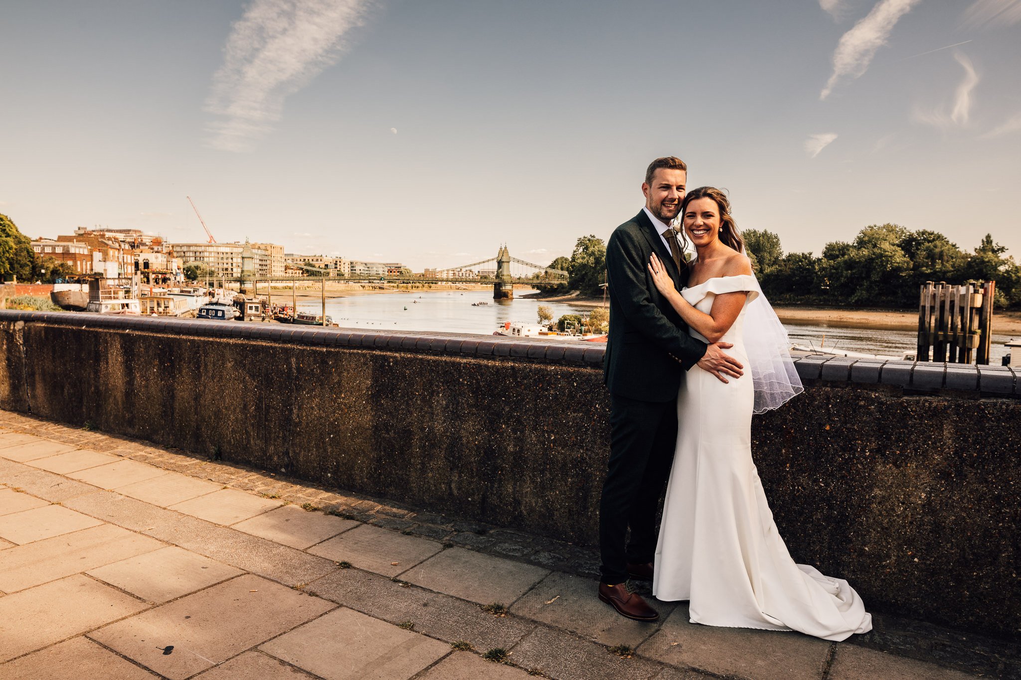  Bride and Groom holding each other on the Thames path with Hammersmith Bride in the background 