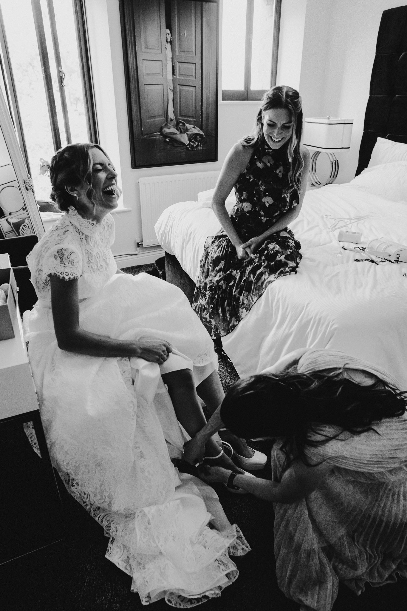  Bride laughing as her bridesmaid puts on her wedding shoes 