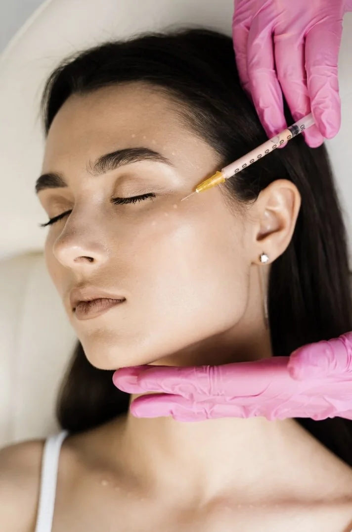 Person receiving cosmetic injection near eye, with pink gloves