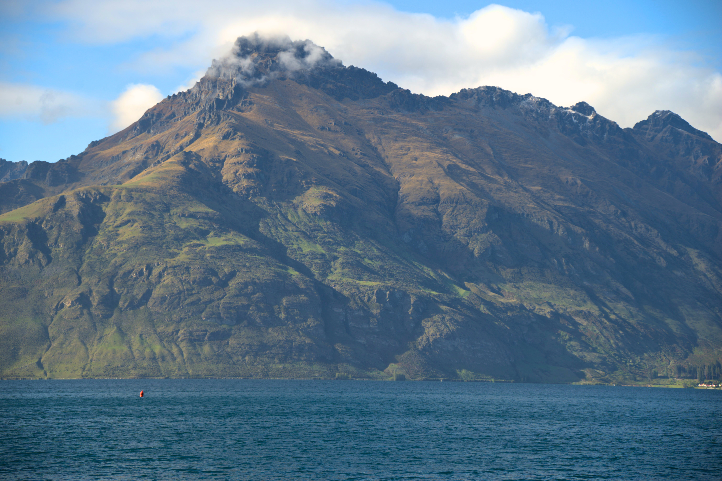 A large mountain with a partly cloudy sky and a body of water in the foreground.