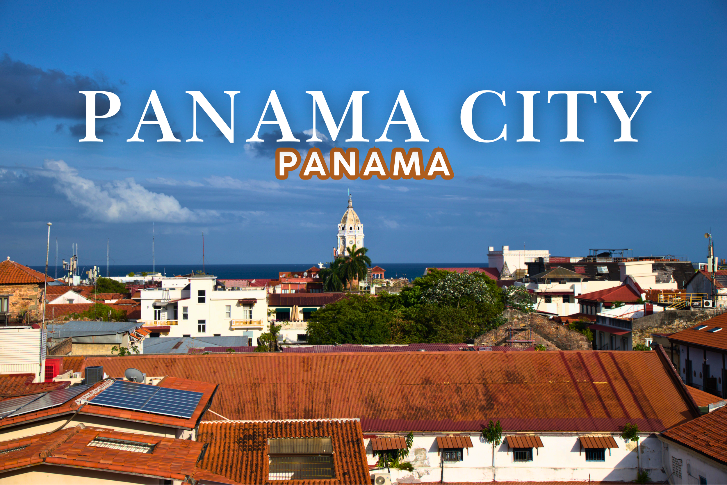 Panoramic view of Panama City with red-tiled roofs, a clock tower, and the ocean in the background under a partly cloudy sky.