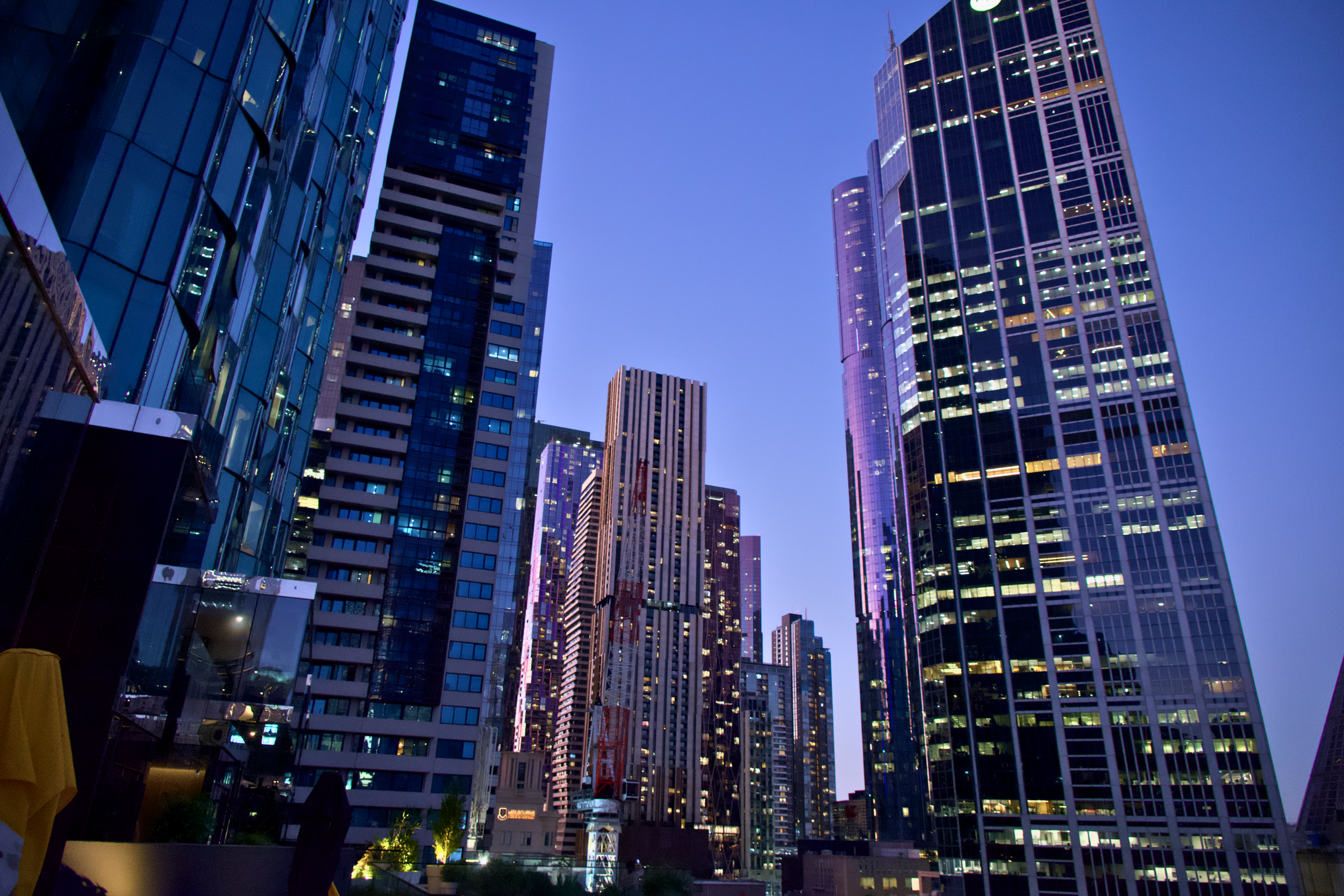 Nighttime view of tall illuminated skyscrapers in a city skyline with purple-lit exteriors and lit windows.