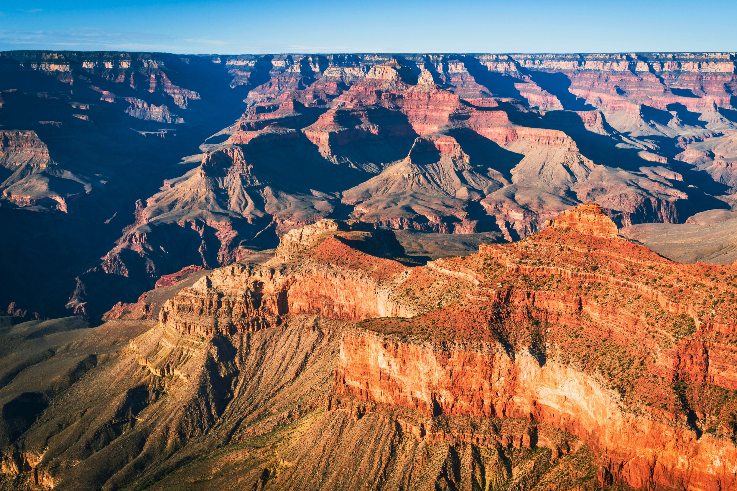 Aerial view of the Grand Canyon showcasing layered red, orange, and brown rock formations under a clear blue sky.