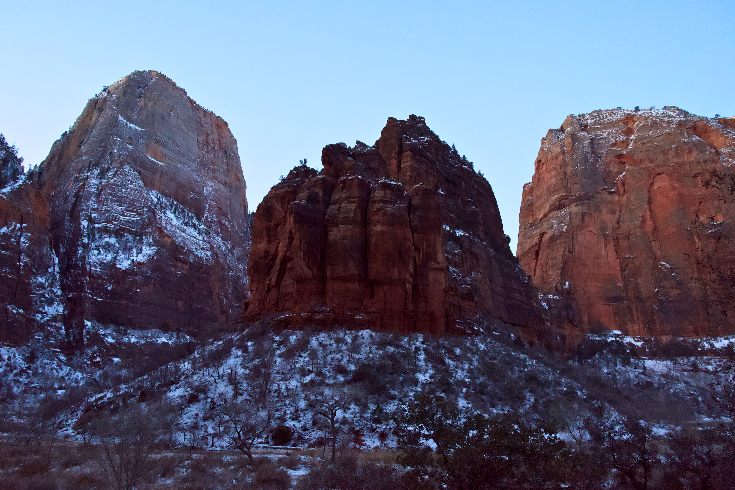 Red rock formations with snow patches under a clear blue sky.