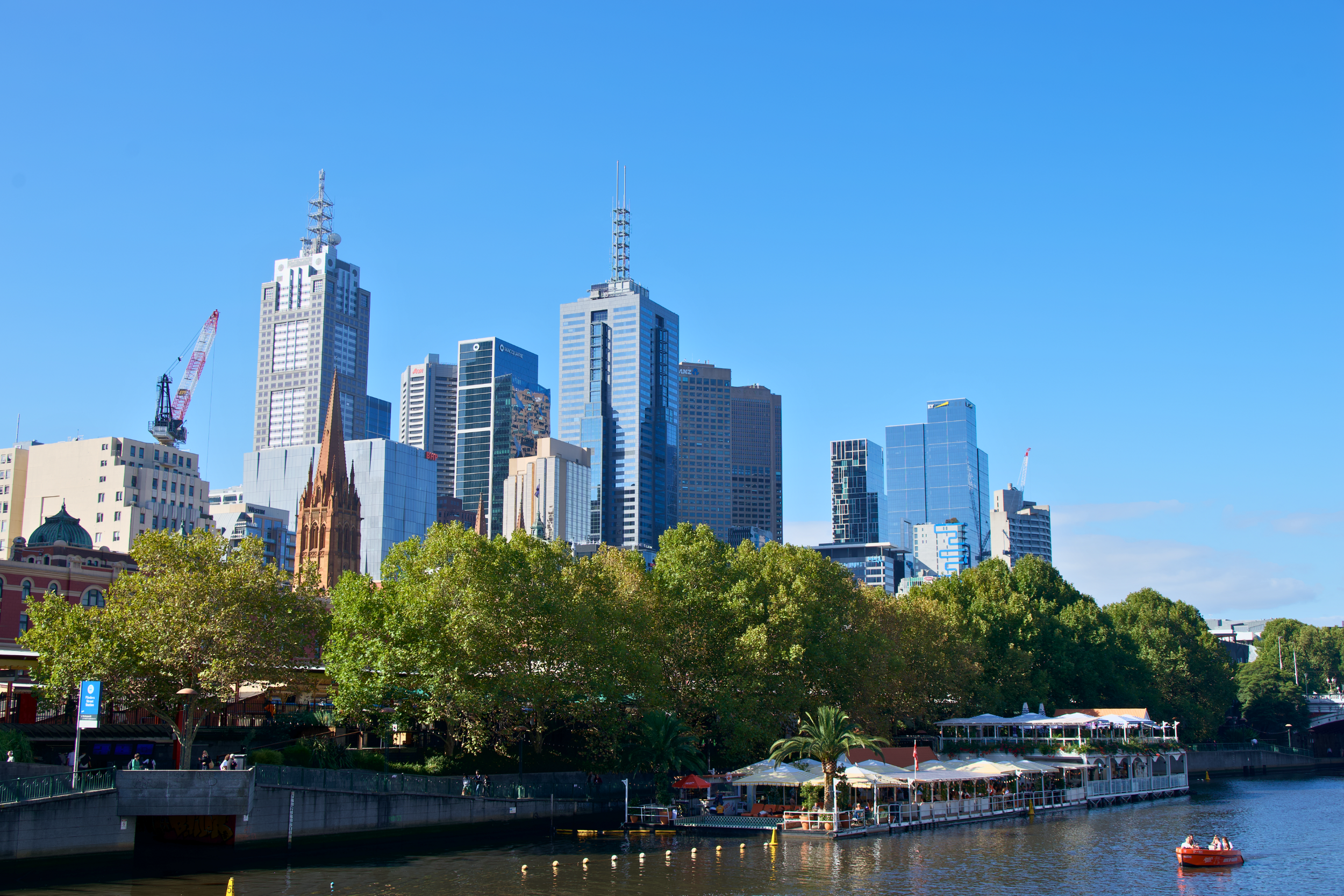 City skyline with skyscrapers, trees, and a river with a boat and a floating restaurant