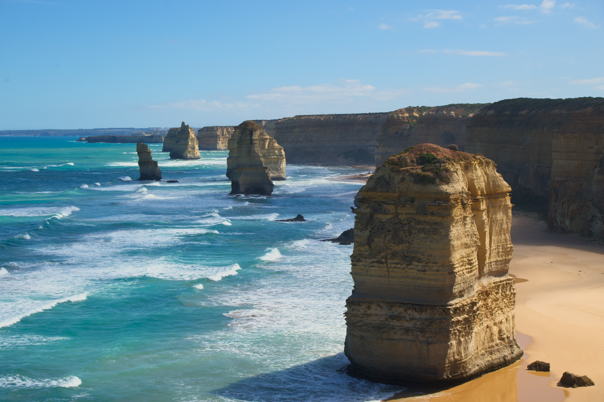 Coastal view of the Twelve Apostles limestone stacks along the Great Ocean Road in Australia, with blue ocean waves and sandy beach.
