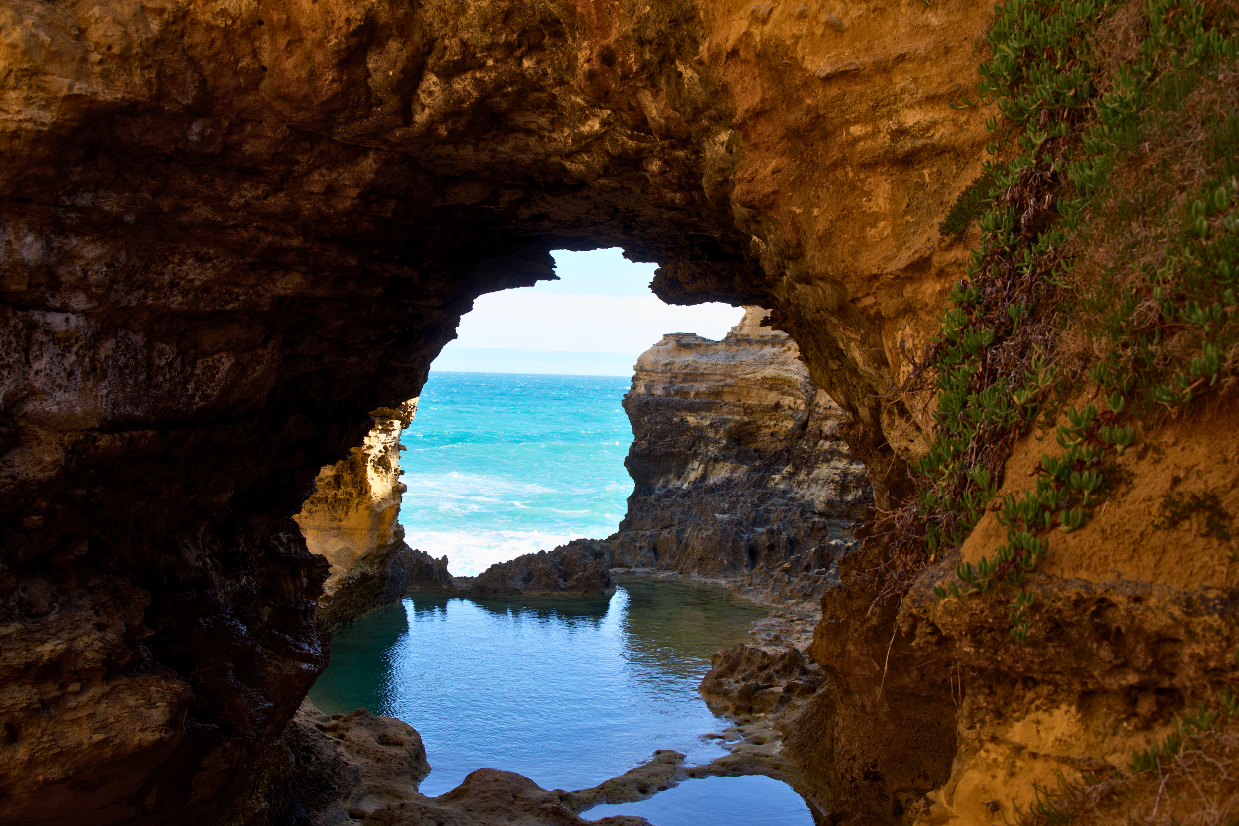 View through a rocky cave opening looking out to the ocean with waves crashing against the rocks.